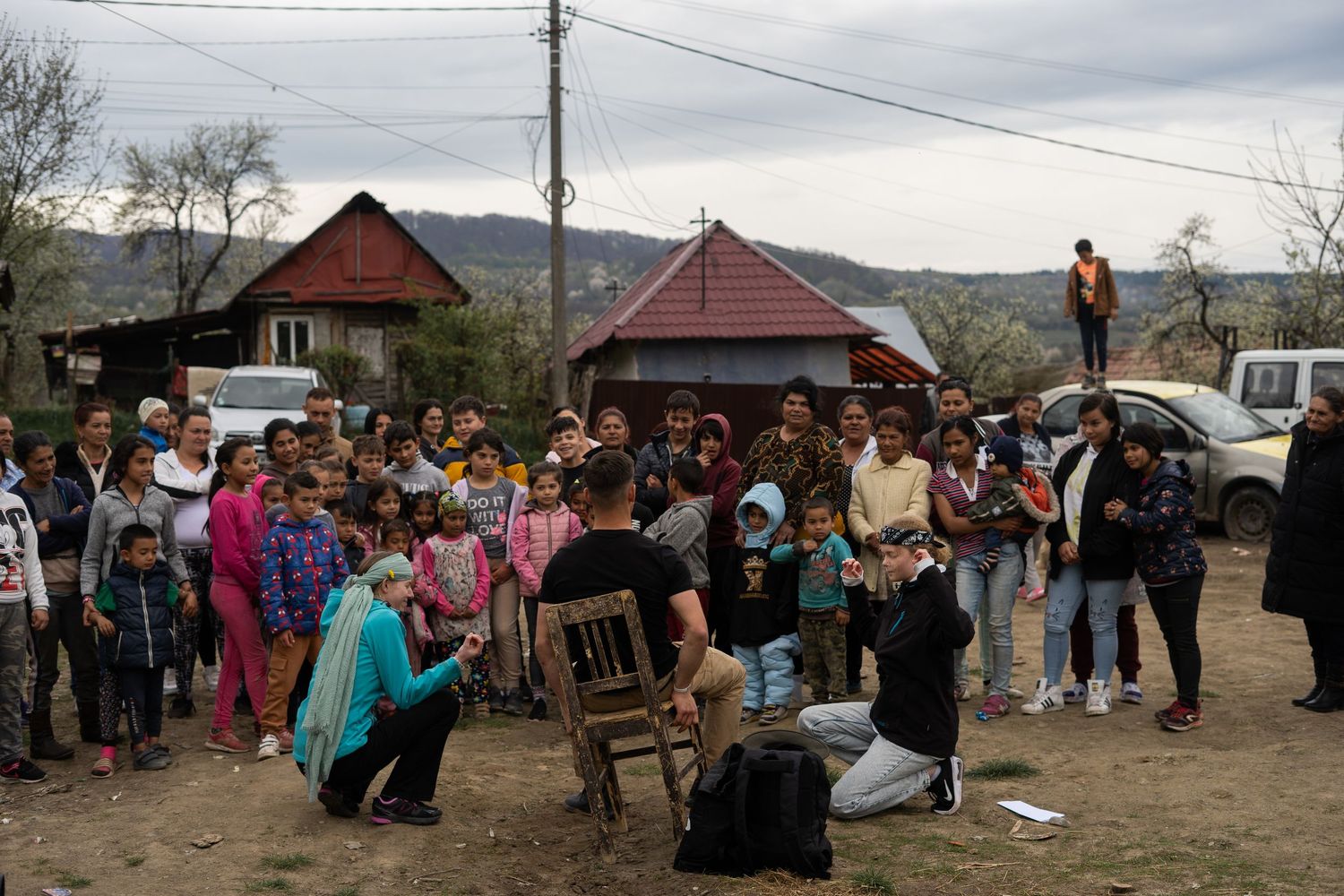 Large crowd of people gathered outdoors in a rural landscape with mountains in the background.