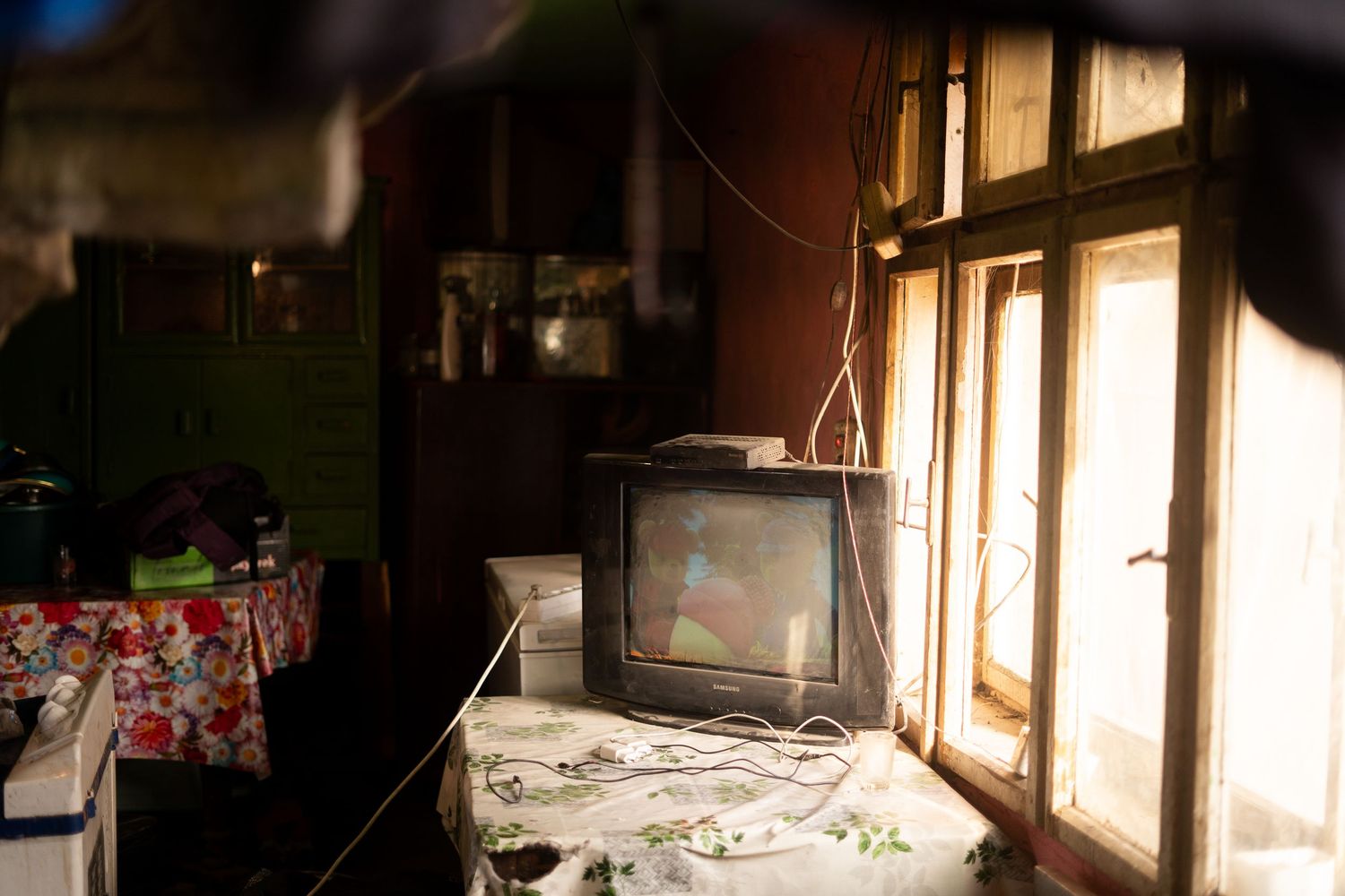 Vintage television set near a window in a dimly lit room with a red and white checkered tablecloth.