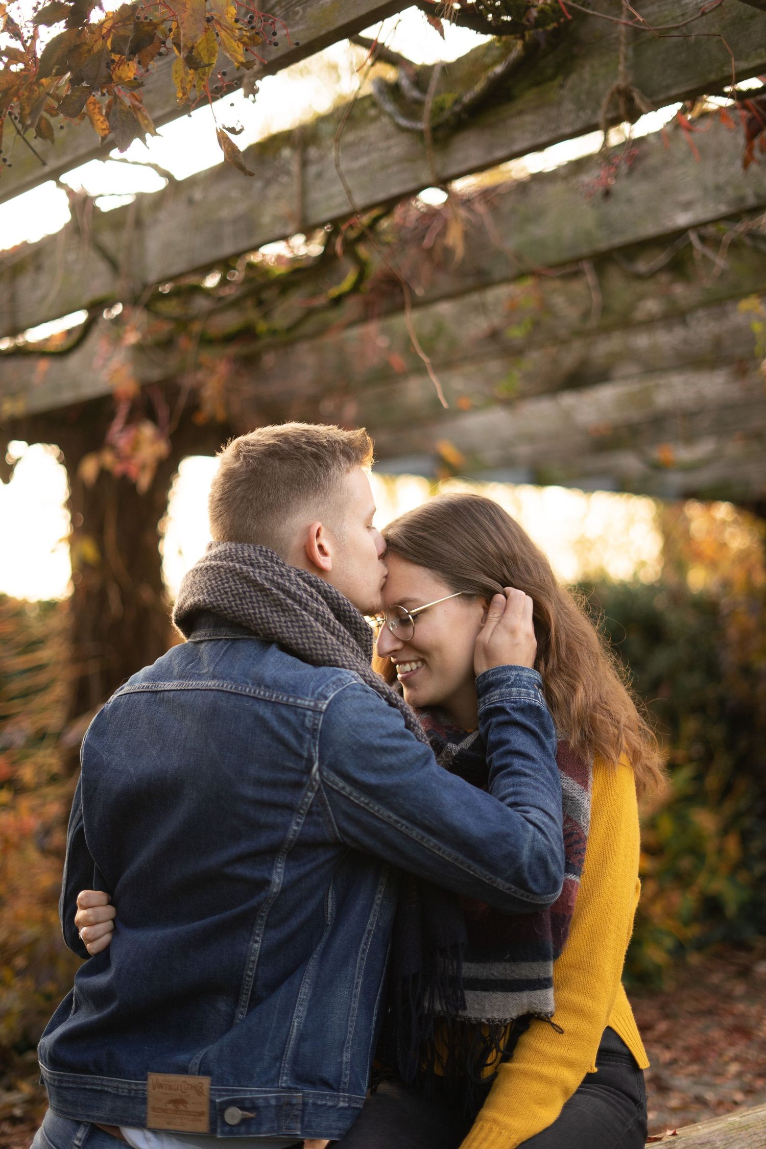 An intimate moment captured between a couple in denim and yellow against autumn foliage.