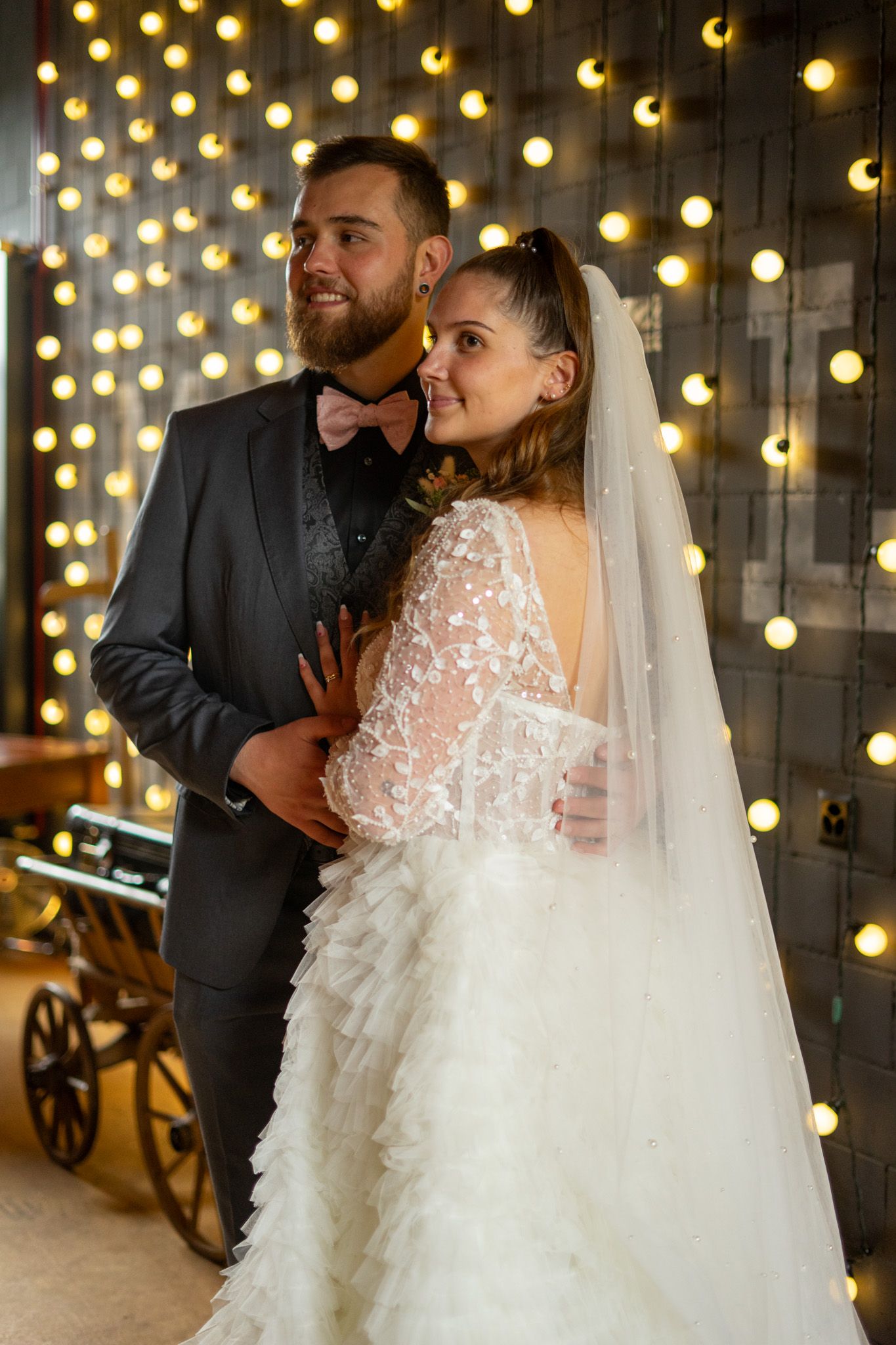 A couple poses against a wall of twinkling lights at their wedding reception.