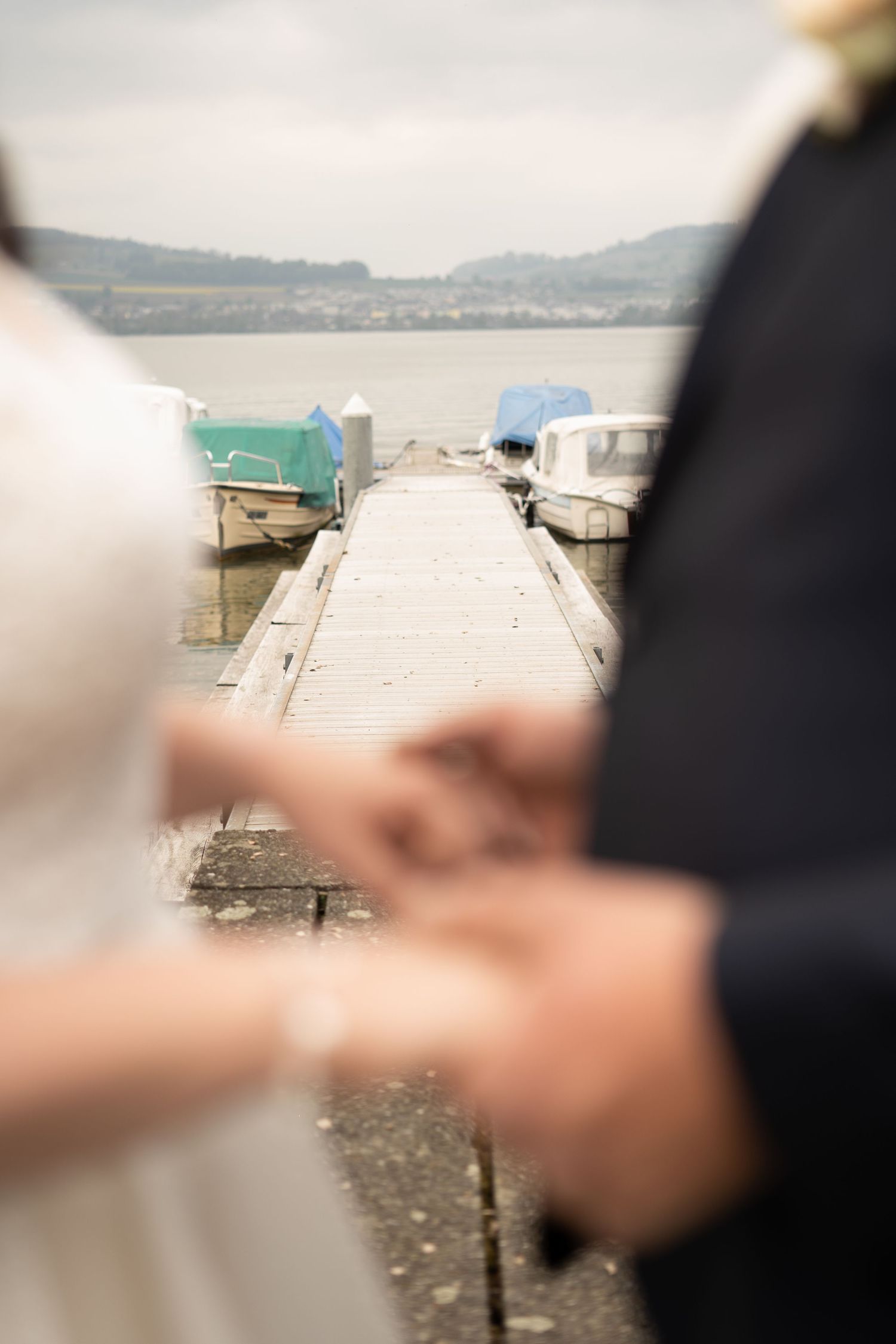 Shallow focus wedding detail shot on a wooden dock with boats in the background.