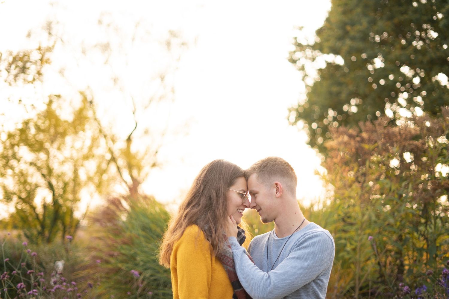 A romantic sunset portrait with soft golden lighting and autumn trees in the background.