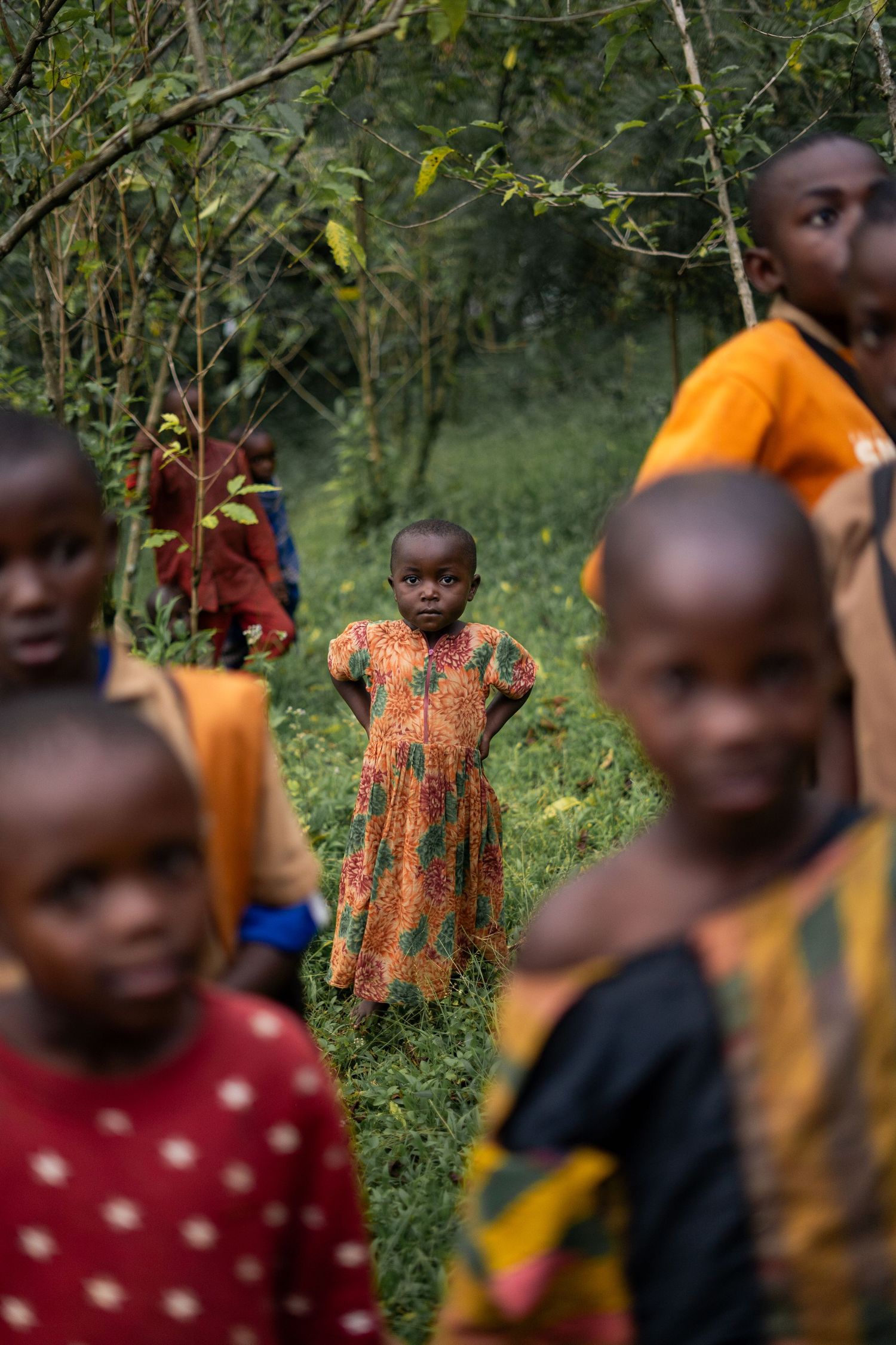 Group of children in colorful clothing standing together in lush green forest setting.