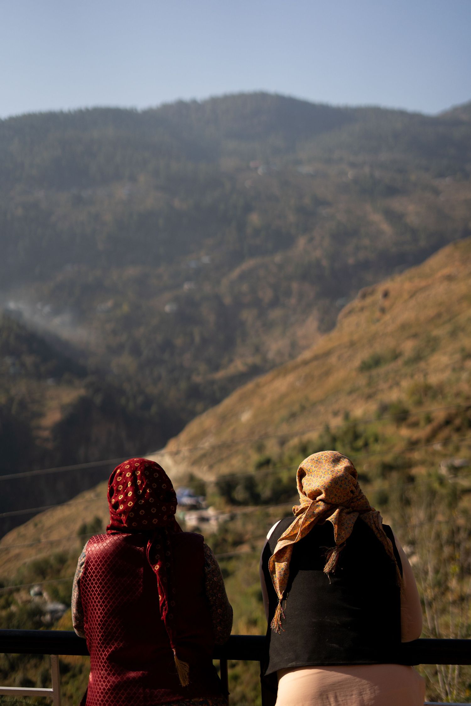 Silhouettes of covered figures sitting against a backdrop of mountainous terrain.