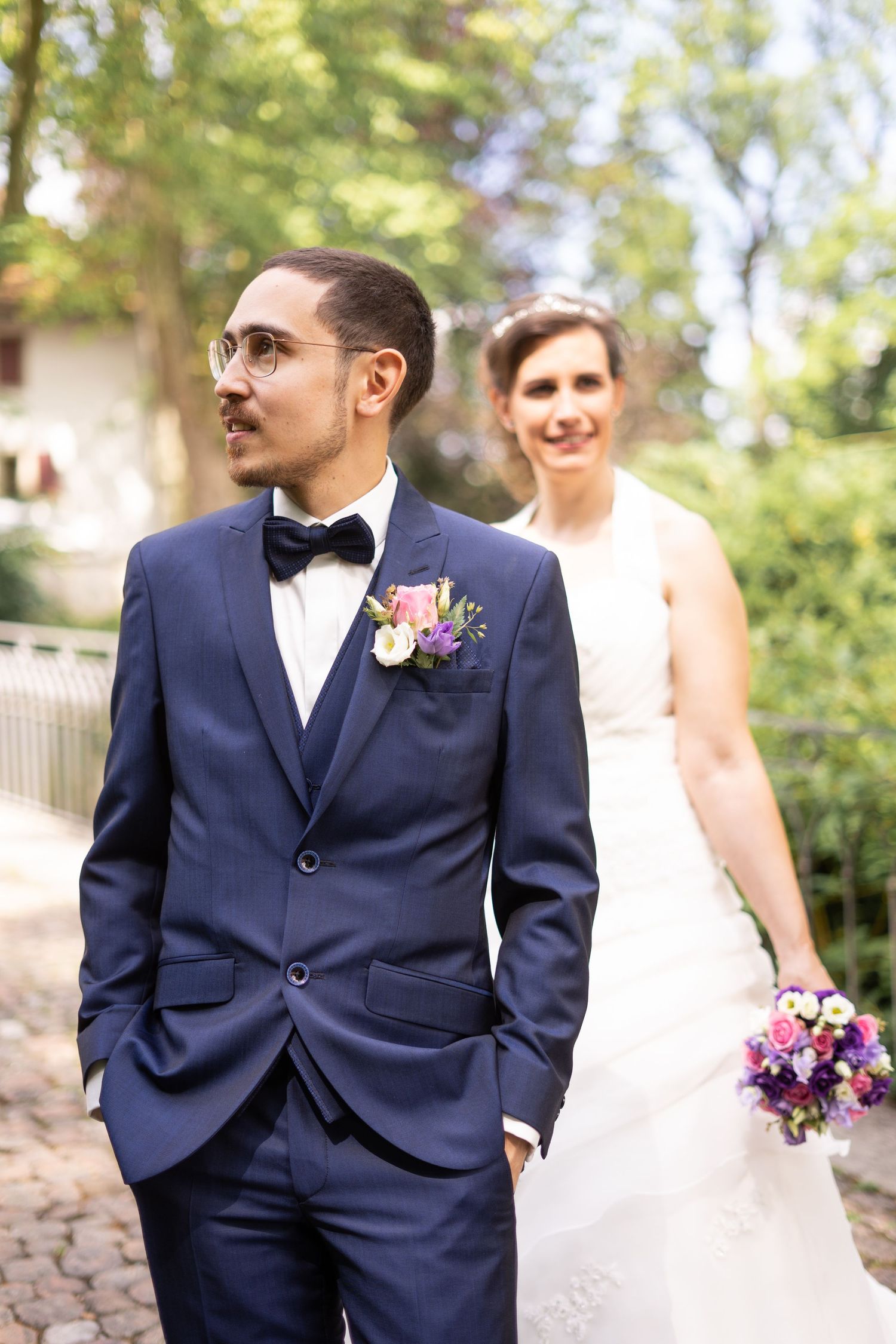 A wedding couple poses on a cobblestone path surrounded by greenery.