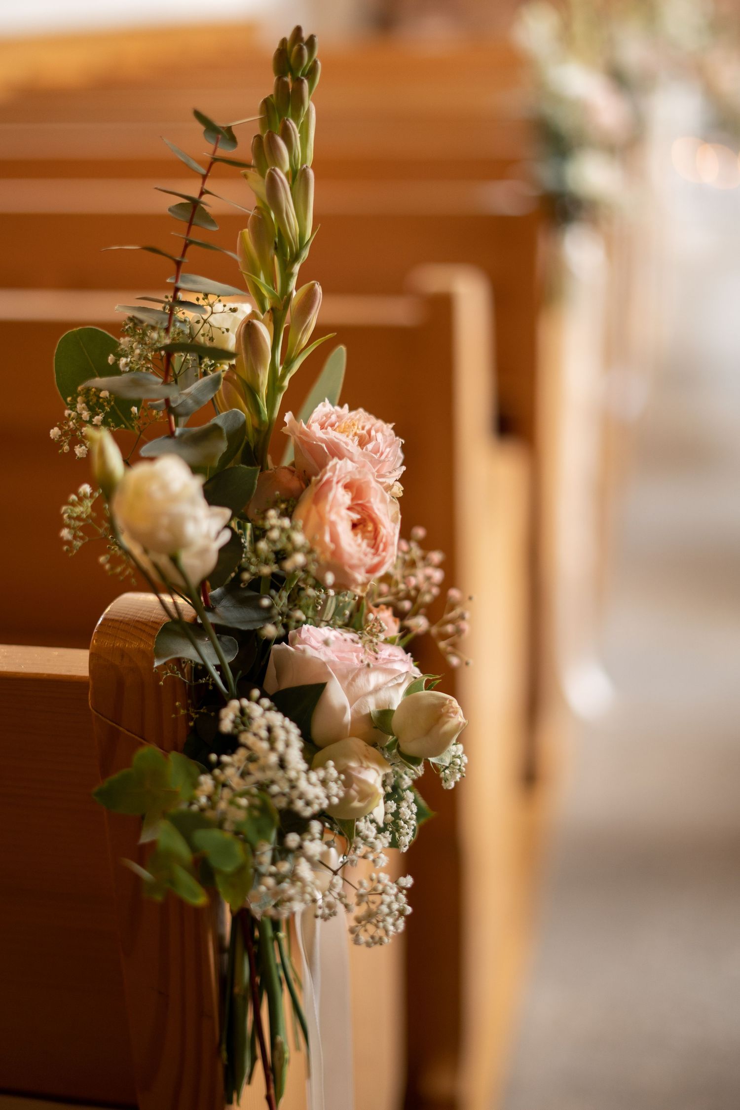 Beautiful floral church pew decoration with pink roses and baby's breath for a wedding ceremony.