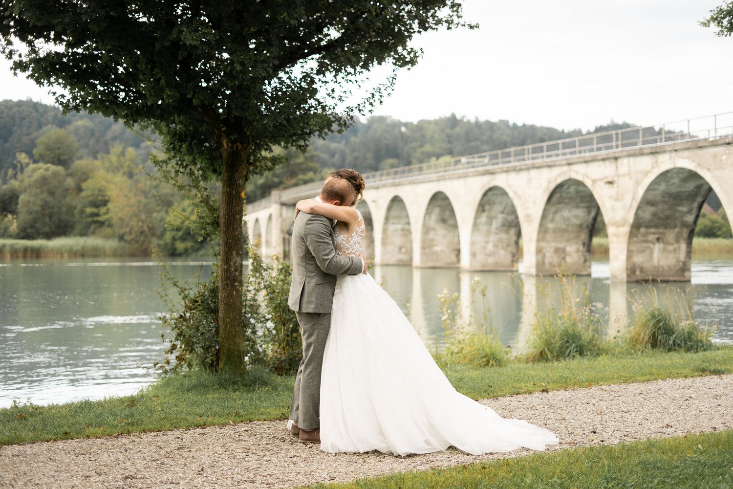 A couple shares a romantic moment by a stone bridge over water during their wedding photoshoot.