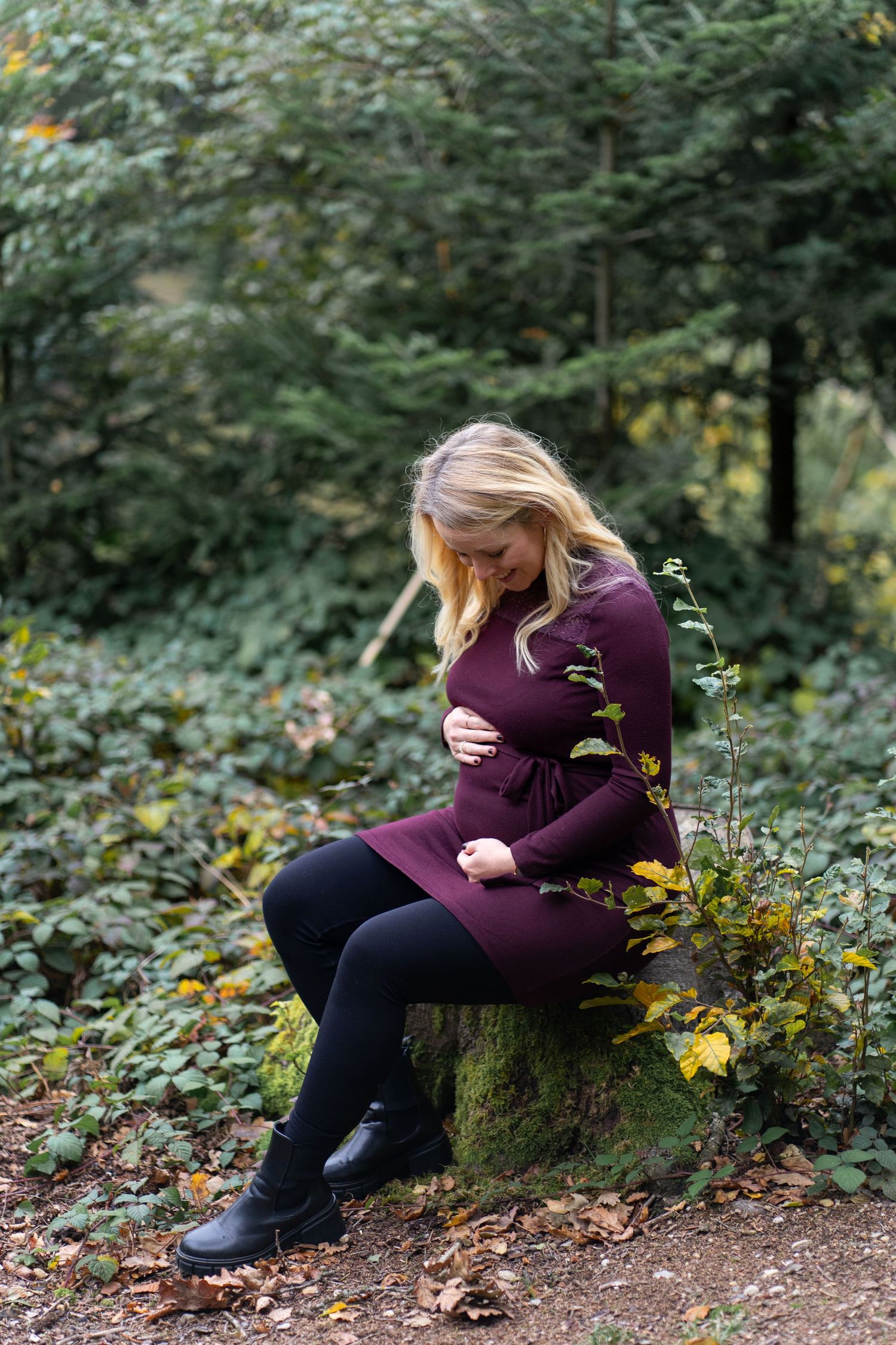 A person sits alone on a tree stump in a wooded area surrounded by autumn foliage.