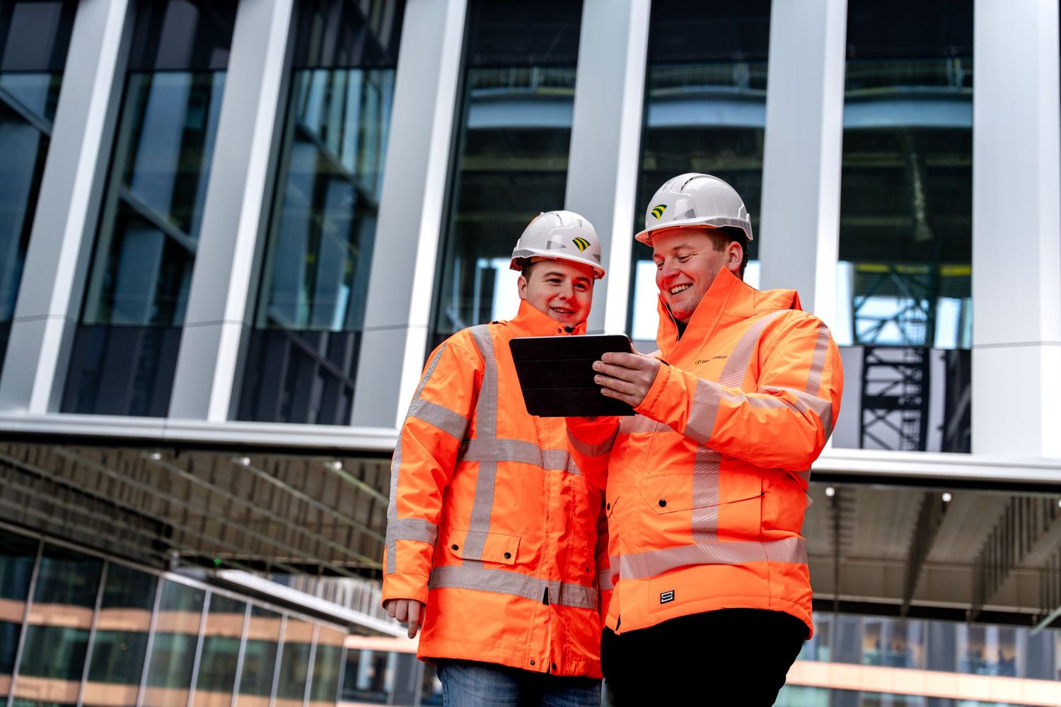 Construction workers in orange safety vests and hard hats inspect work progress at a building site. - Noelle Schmeltz Fotografie