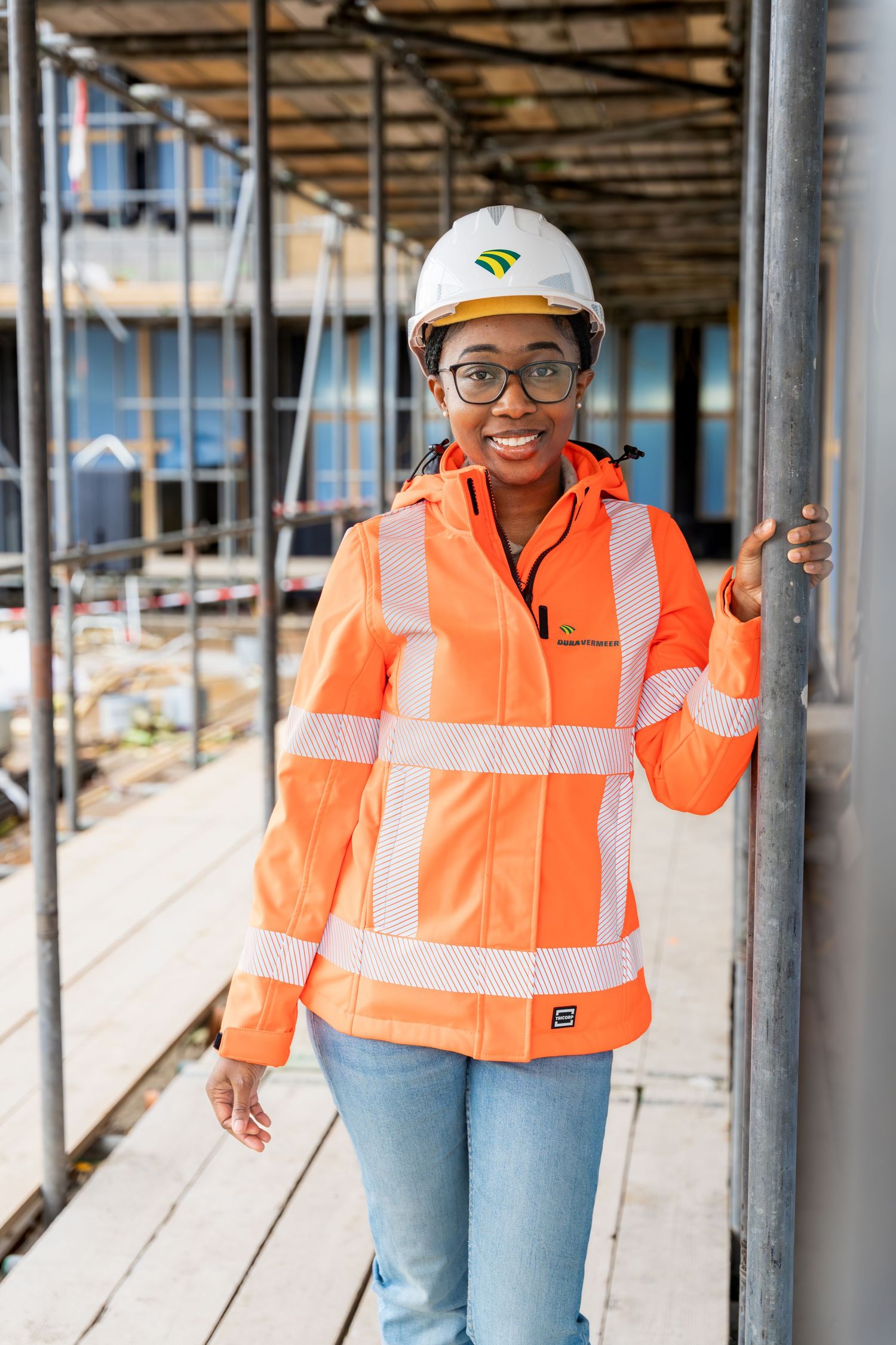 Construction workers in high visibility orange safety vests and hard hats smiling at a building site. - Noelle Schmeltz Fotografie