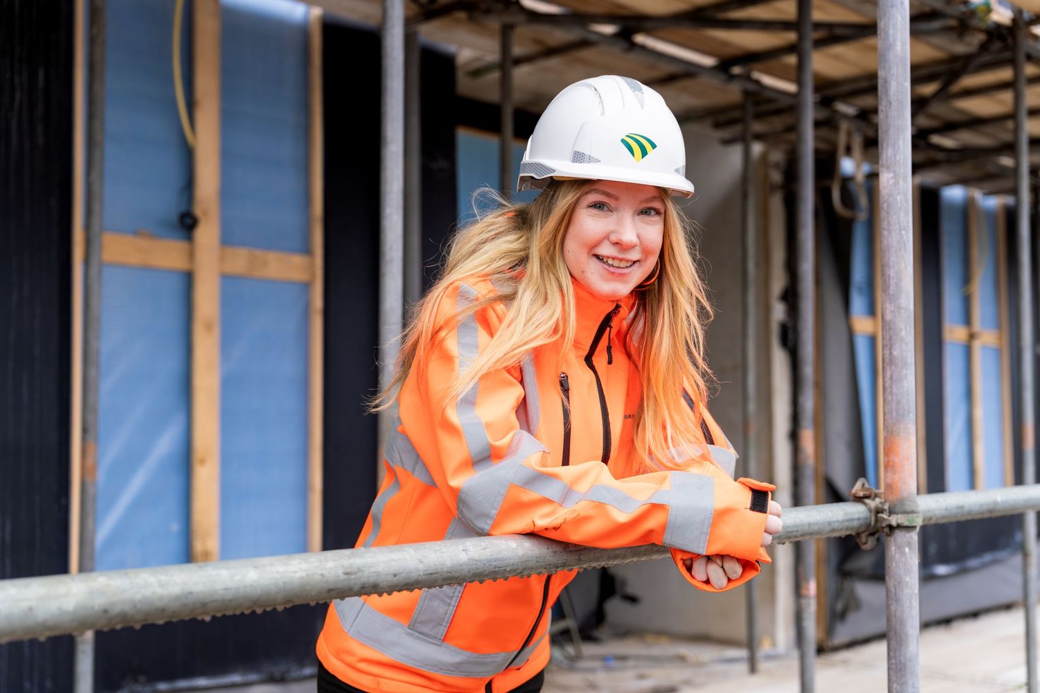 Construction worker in orange safety vest and hard hat smiles while working at a building site. - Noelle Schmeltz Fotografie