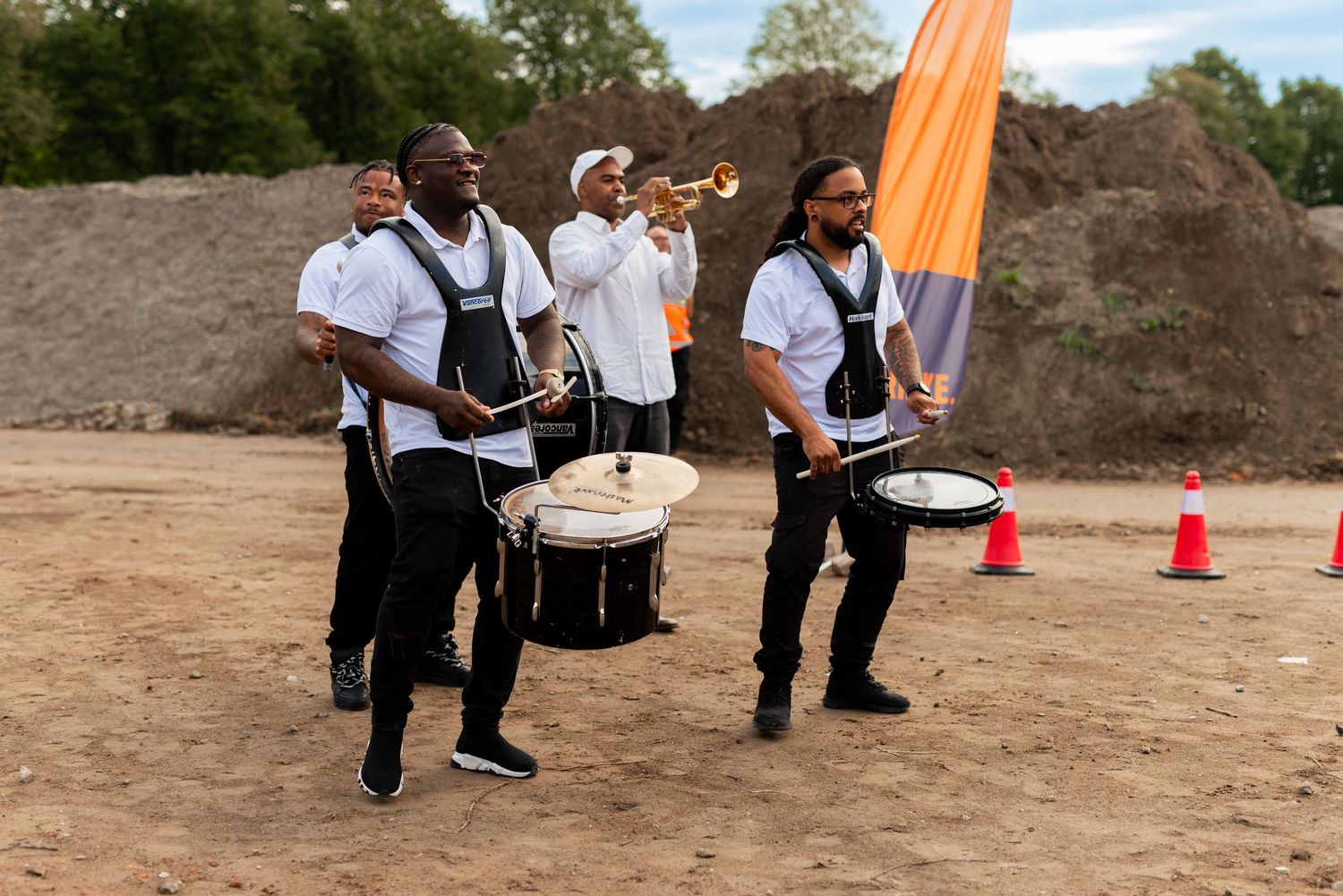 Musicians perform with drums and flag on a dirt field during an outdoor event.  - Noelle Schmeltz Fotografie