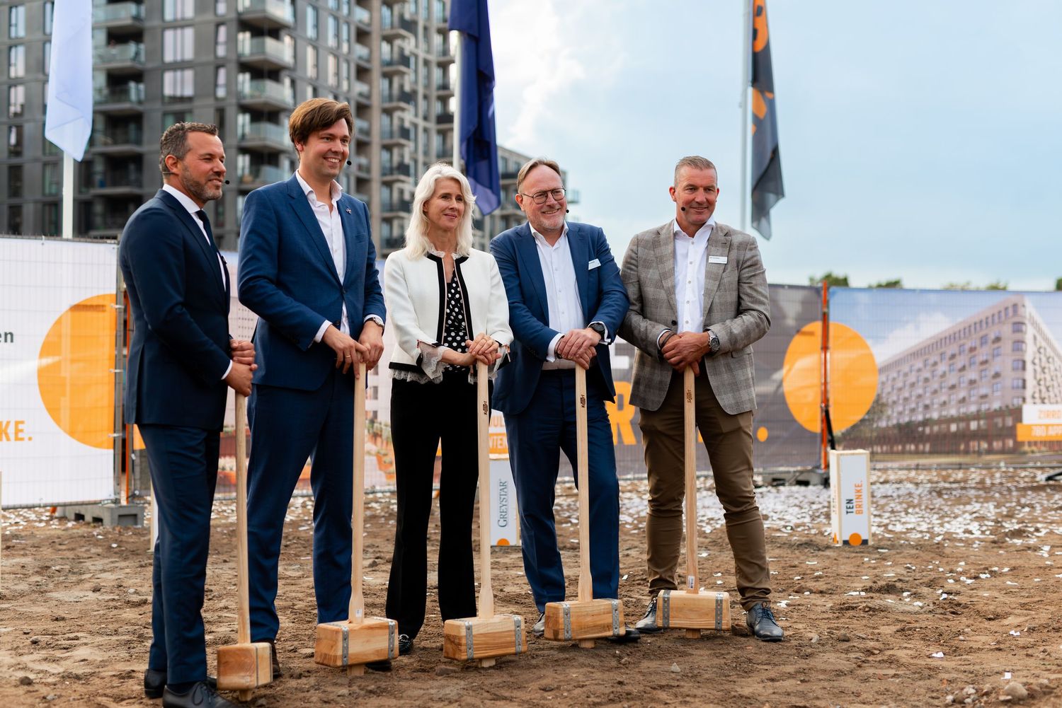 A group of business professionals with shovels stands at a construction site groundbreaking ceremony. - Noelle Schmeltz Fotografie
