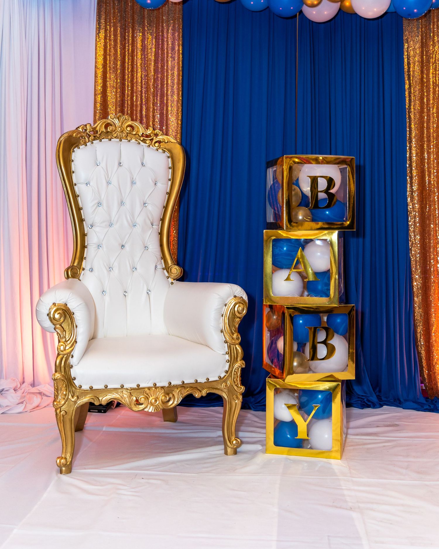 Elegant white tufted armchairs with gold frames arranged in front of blue drapes for a formal event.