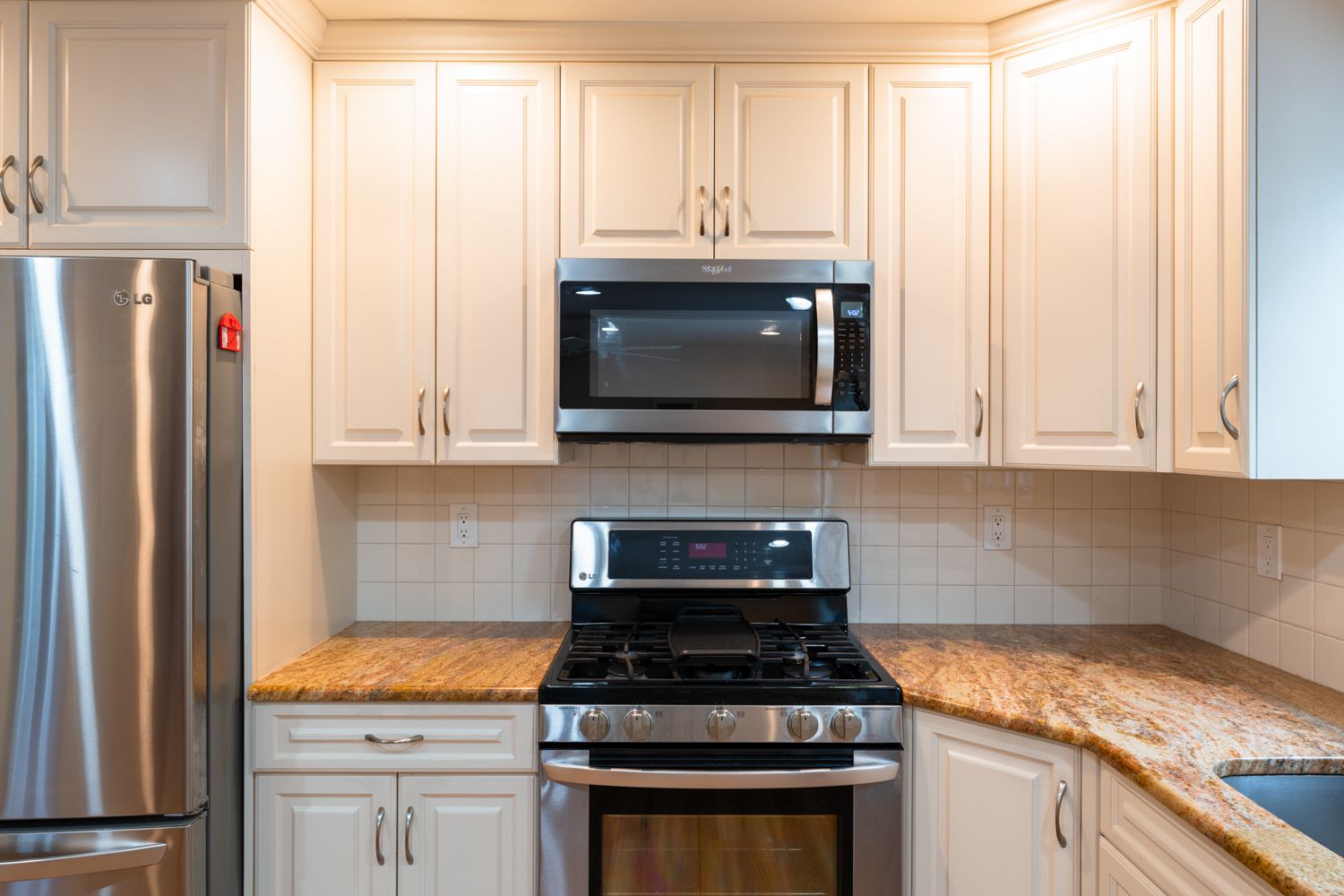 Modern white kitchen with granite countertops, stainless steel appliances, and recessed lighting features elegant cabinetry.