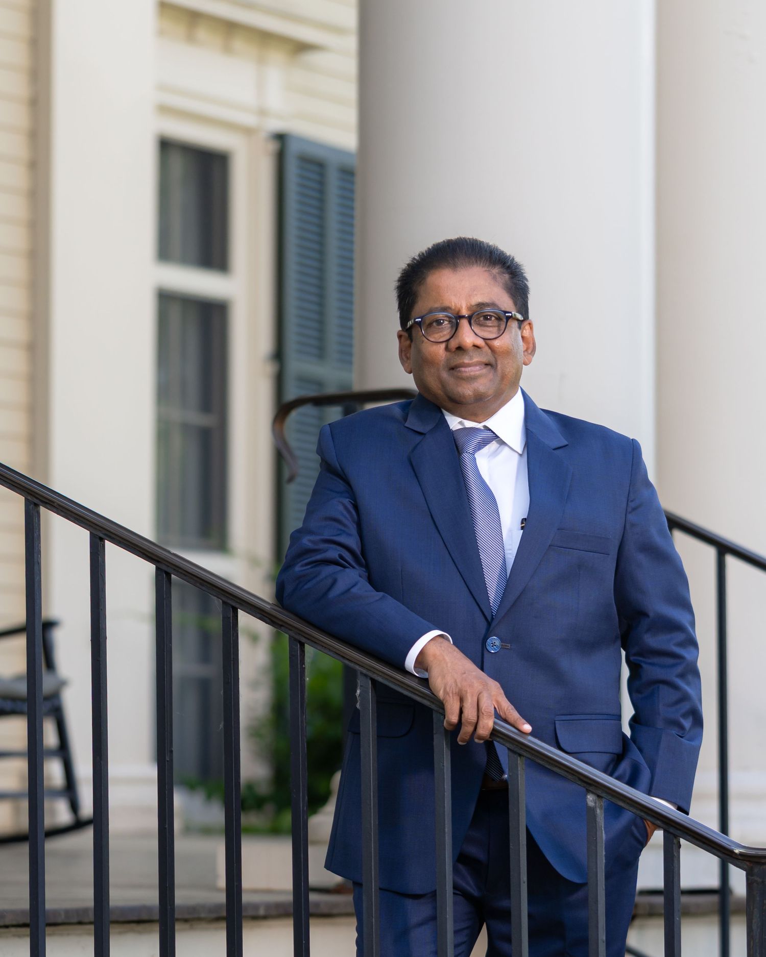 Professional in navy blue suit poses on white building steps with railing.