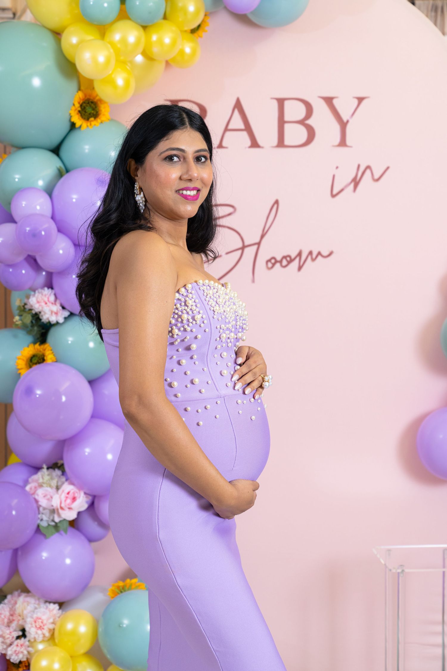 Baby shower setup with purple and yellow balloon arrangements against pink backdrop.