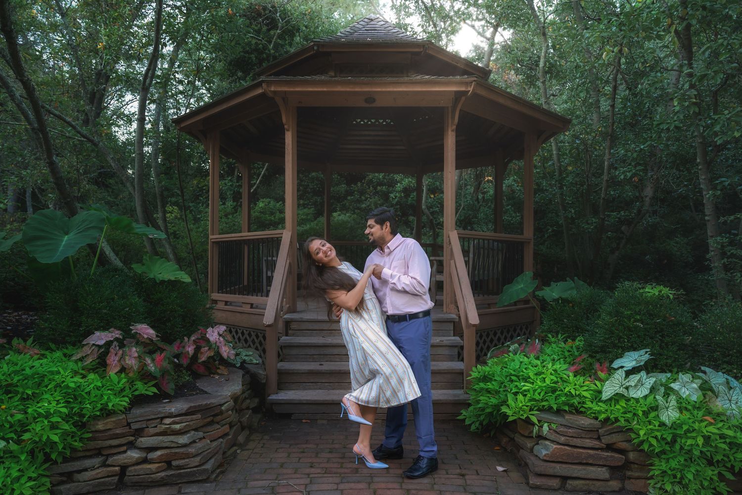 Romantic couple sharing playful moments in a rustic wooden gazebo surrounded by lush greenery.