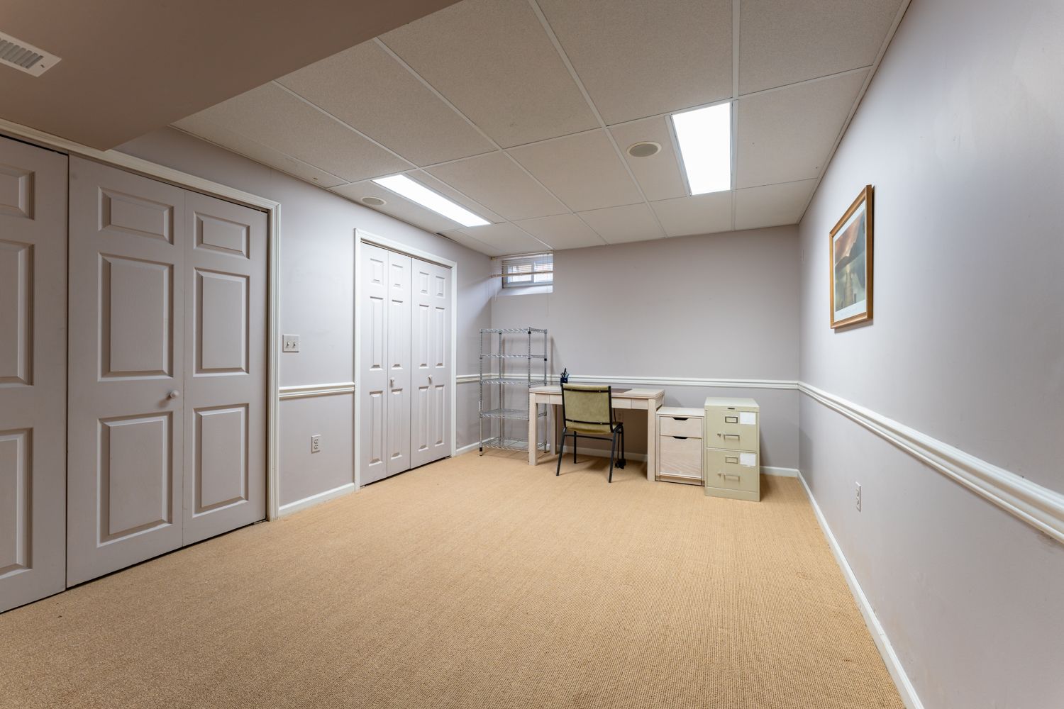 Long empty hallway with white walls, beige carpet, and fluorescent lighting showing multiple closed doors.