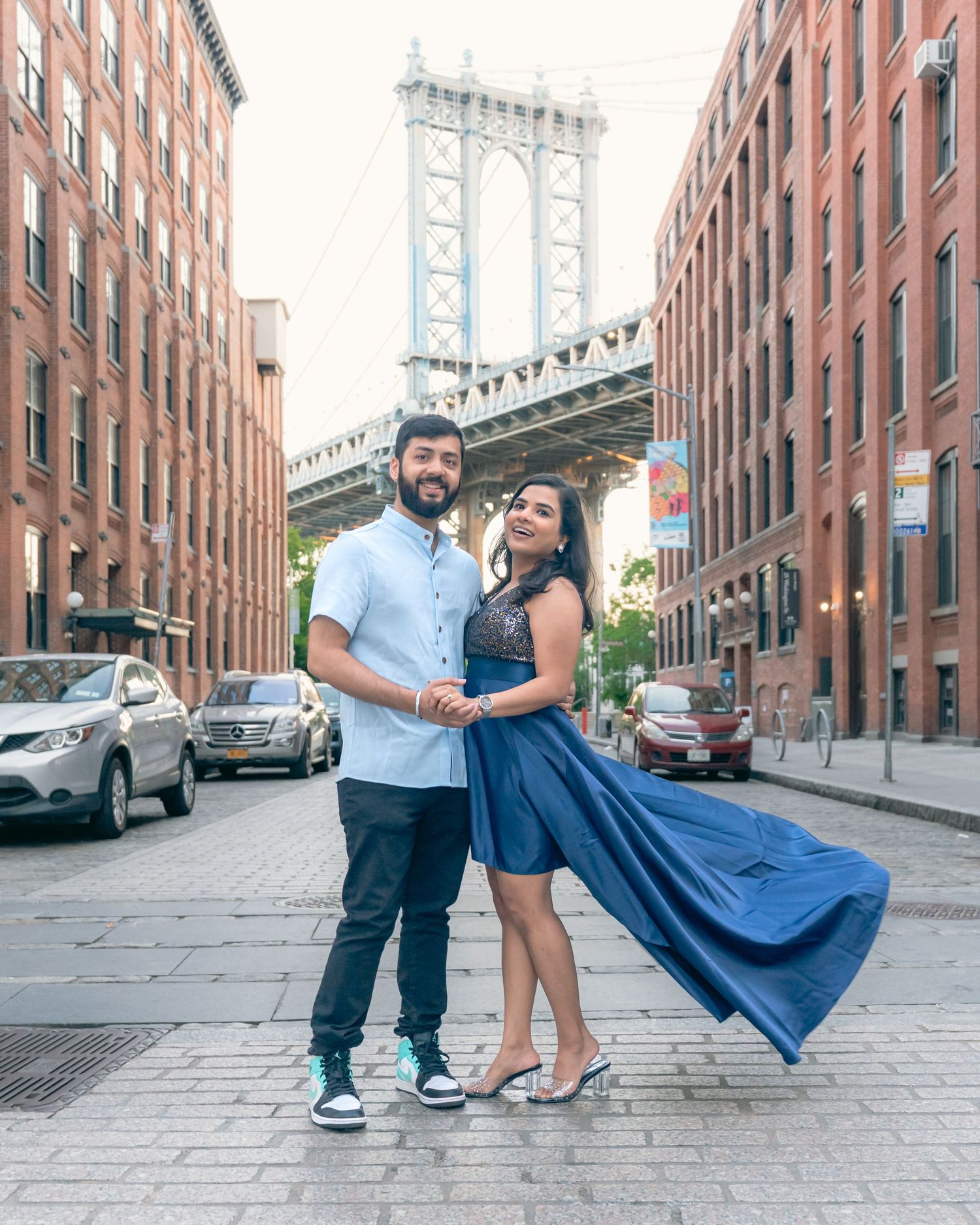 A couple poses on a Brooklyn street with the Manhattan Bridge visible in the background.