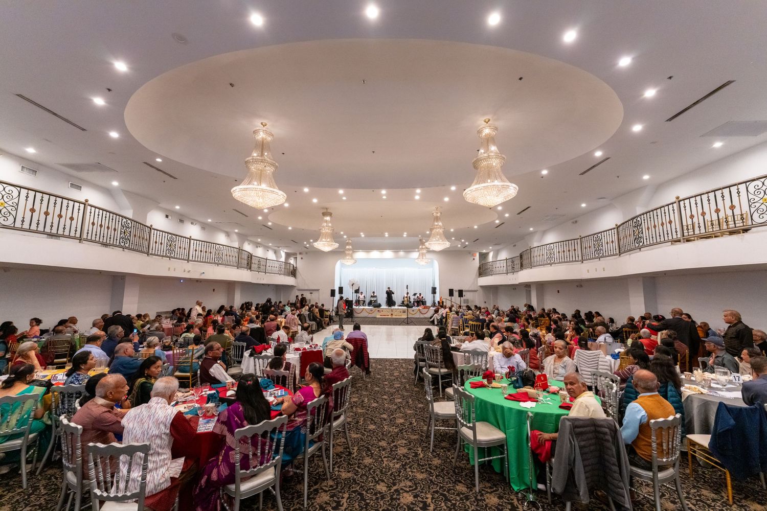Large panoramic view of a crowded conference room with attendees seated at round tables under crystal chandeliers.