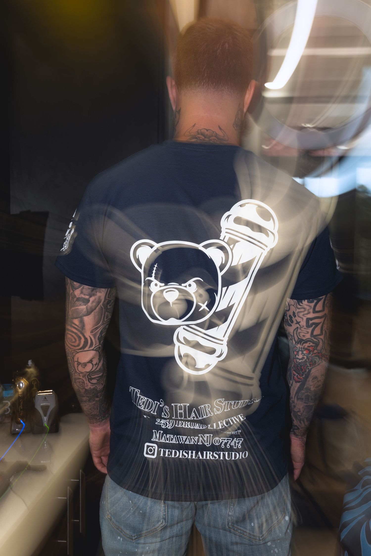 Back view of a navy blue t-shirt with custom printed logo design worn in a barbershop setting.