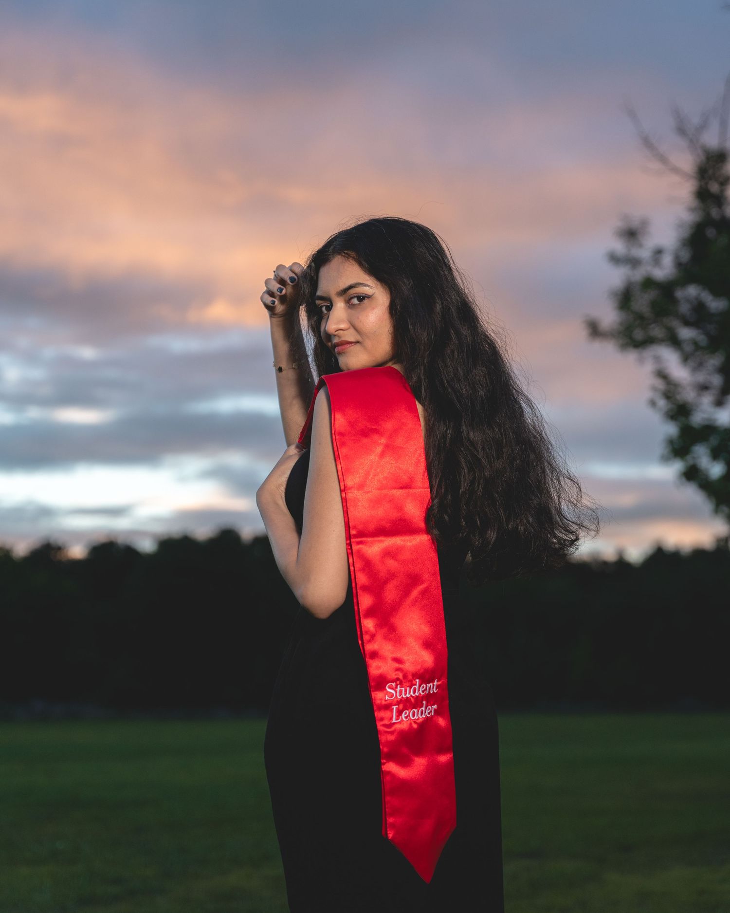 A red graduation sash photographed against a sunset sky in the background.