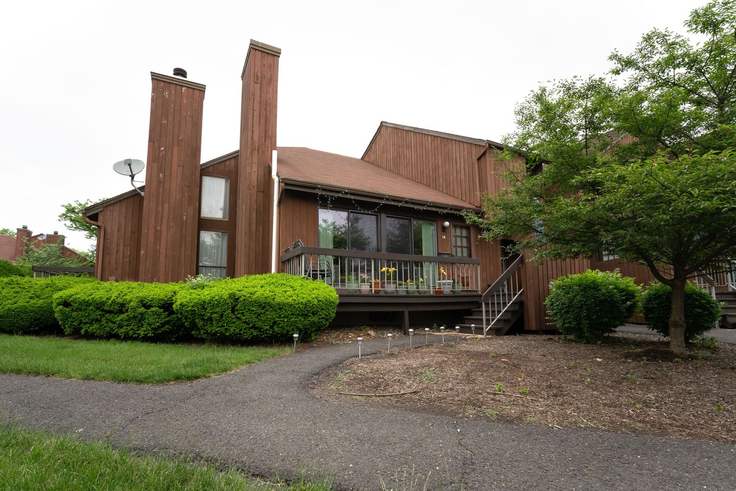 A row of modern residential buildings with brown exteriors sits nestled among green trees and landscaping.