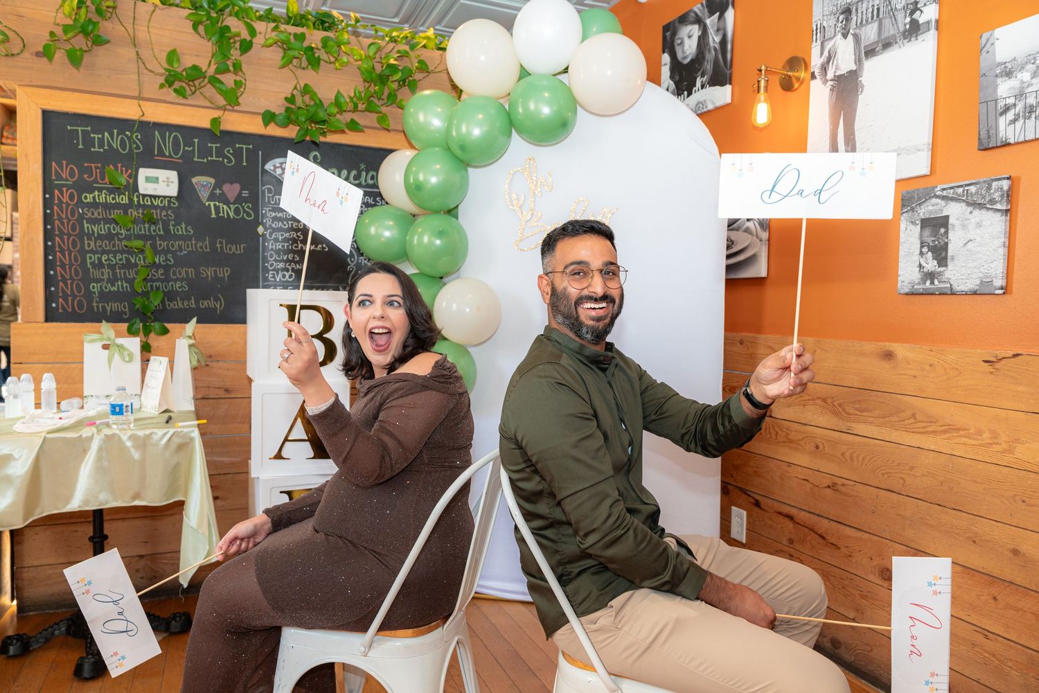 People celebrating at a casual restaurant with green and white balloons decorating the interior space.