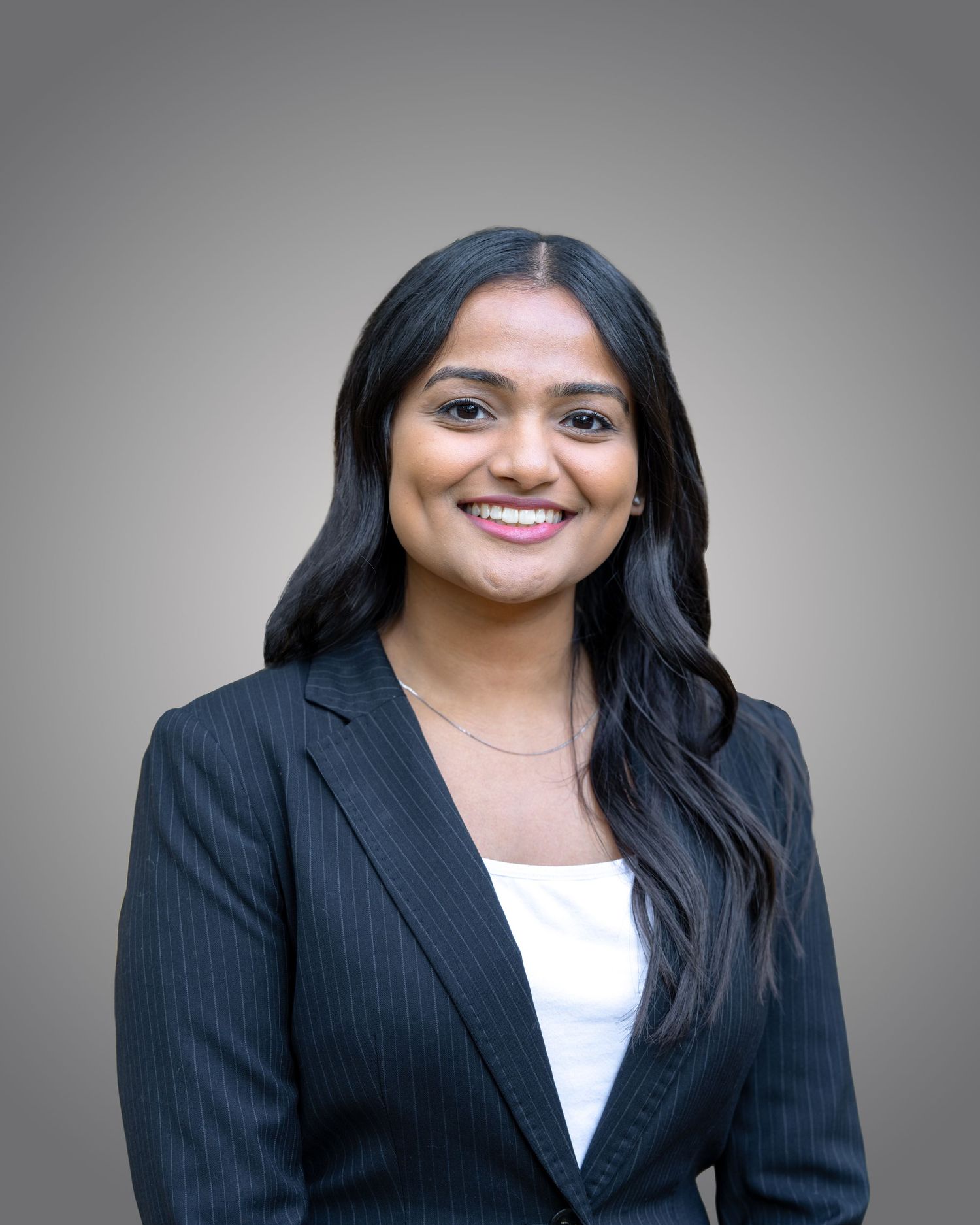 Professional headshot series of a person in a black blazer and white top against a grey background.