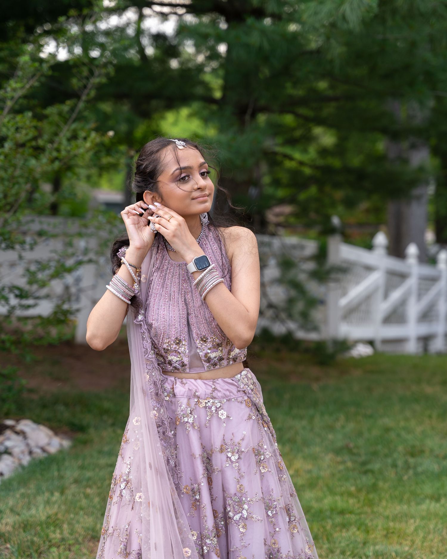 Woman in lavender formal dress with sequins poses in garden setting.