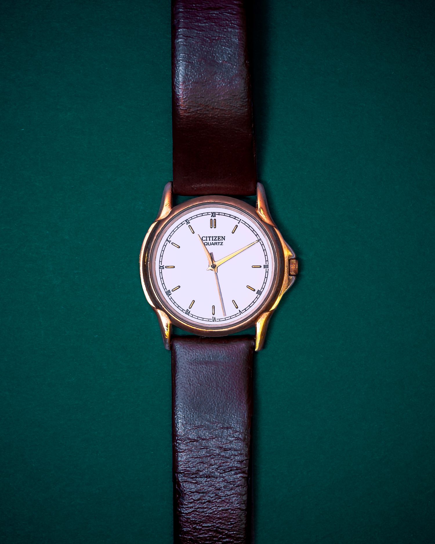 Classic analog watch with brown leather strap displayed against a dark green background.