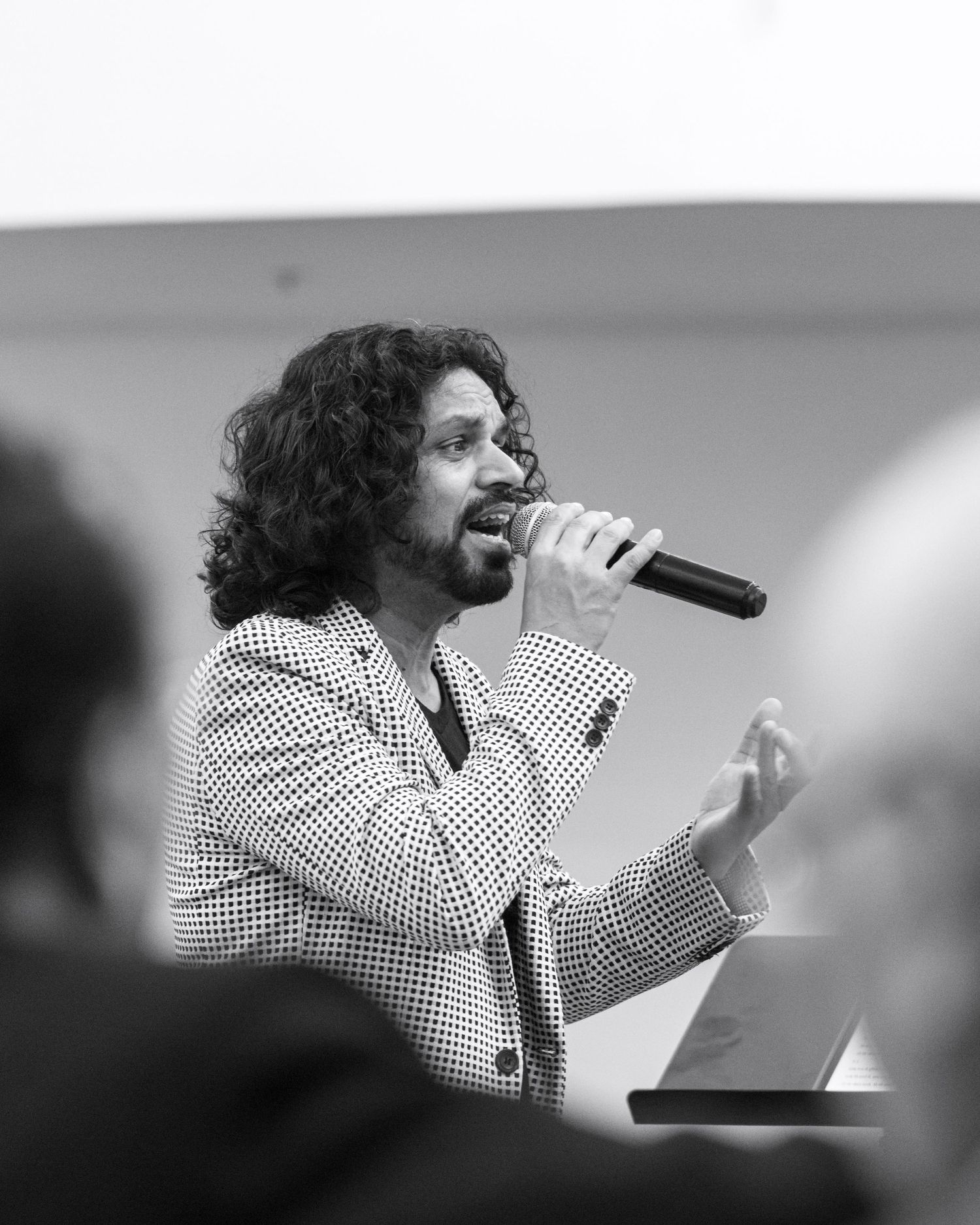 A performer in a polka dot suit sings passionately into a microphone during a black and white performance.