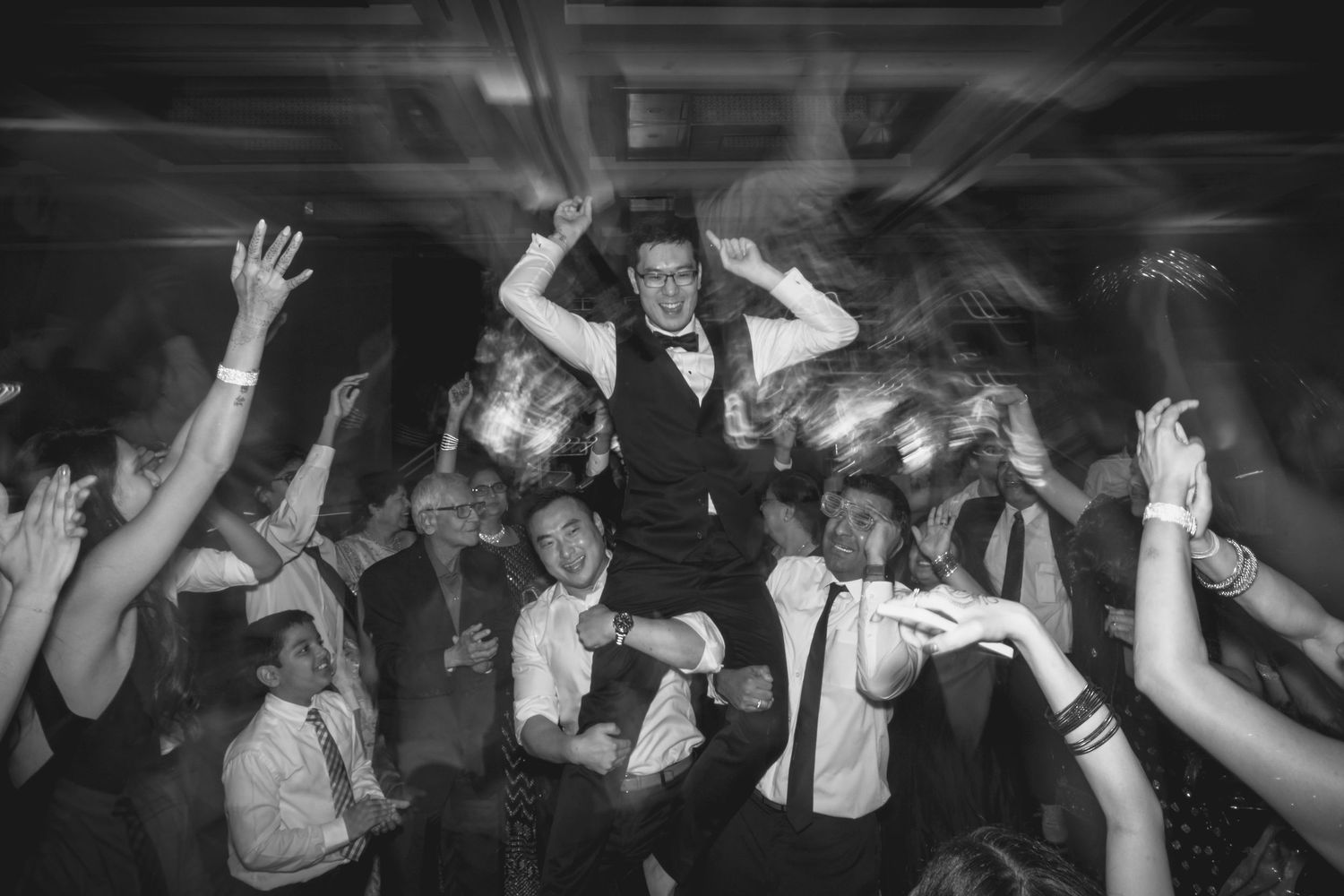 Crowded dance floor with party guests raising their hands in celebration at a nighttime event.