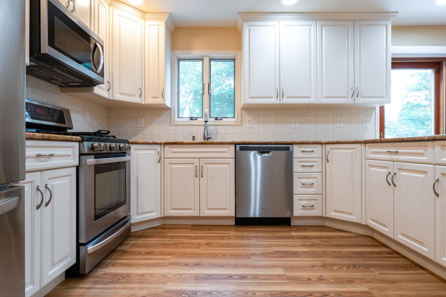 Panoramic view of a spacious L-shaped kitchen with white cabinets and granite countertops showcases modern design.