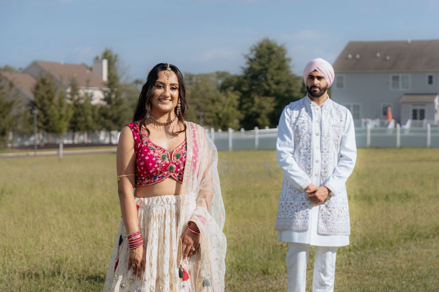 Wedding couple in traditional Indian attire posing in a sunny field.