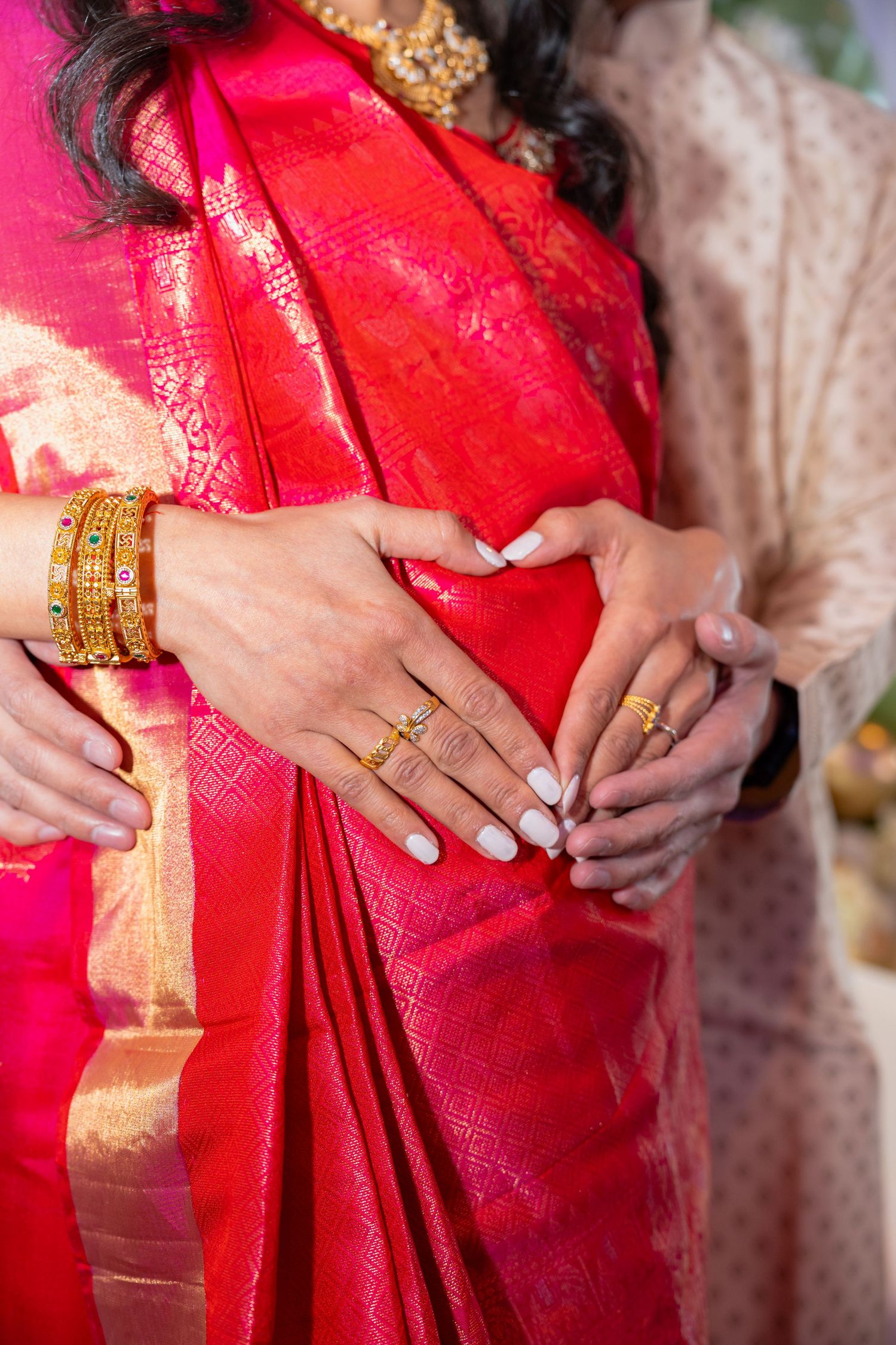 Close-up of hands adorned with gold bangles and rings against a vibrant red and gold silk sari.