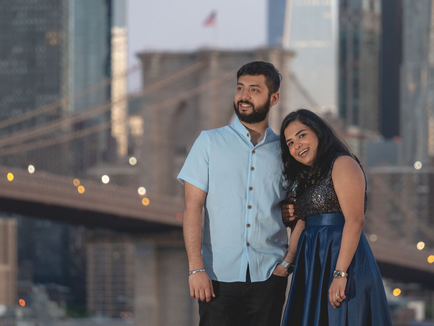 Couple in casual outfits poses for romantic photos with city buildings in background.