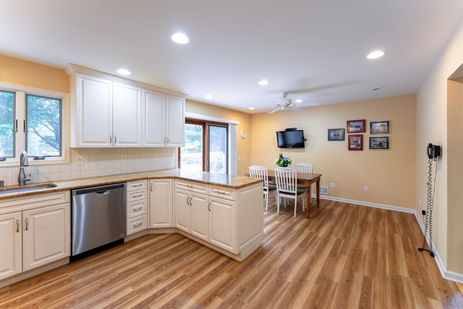 Panoramic view of modern basement renovation with light hardwood floors, white cabinets, and recessed lighting.