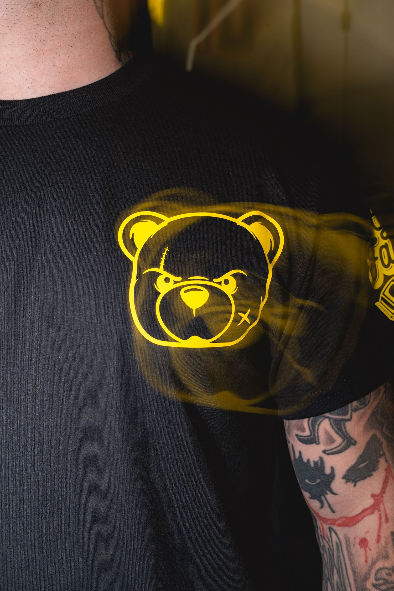 T-shirt design featuring a yellow teddy bear logo on dark fabric in various stages of completion.