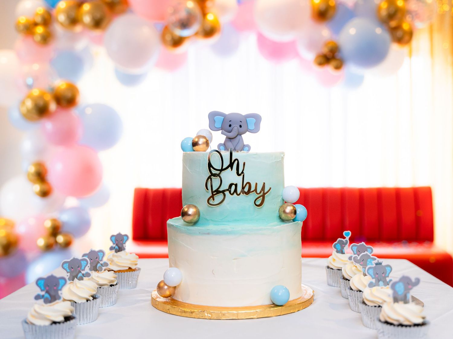 Baby shower decorations featuring blue and pink balloons with a white cake display.