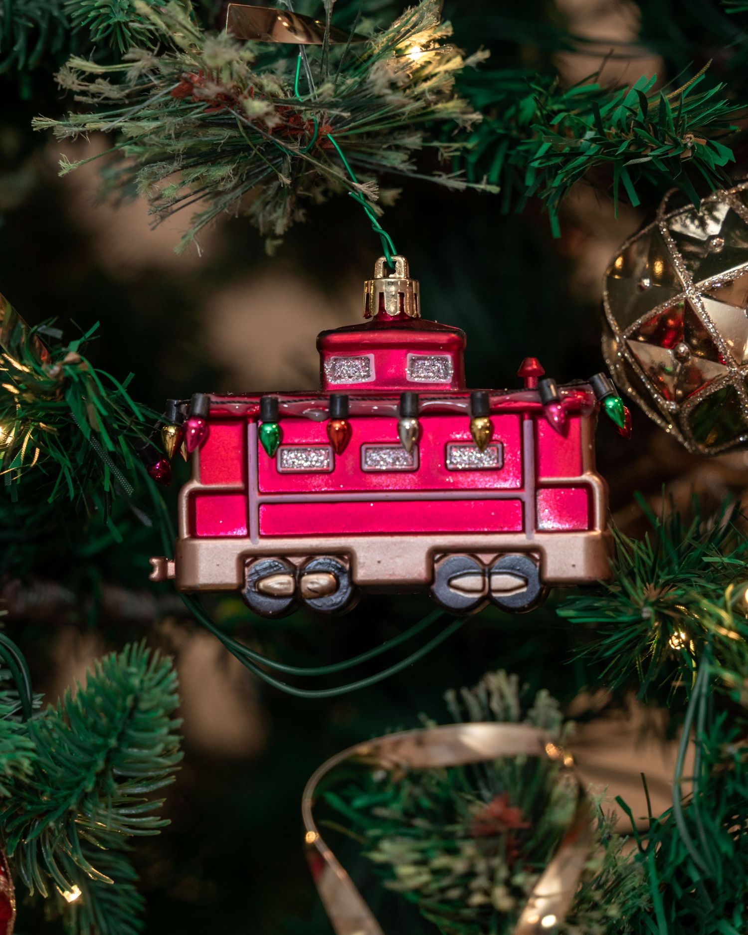 A pink toy train Christmas ornament hanging on an illuminated evergreen tree.