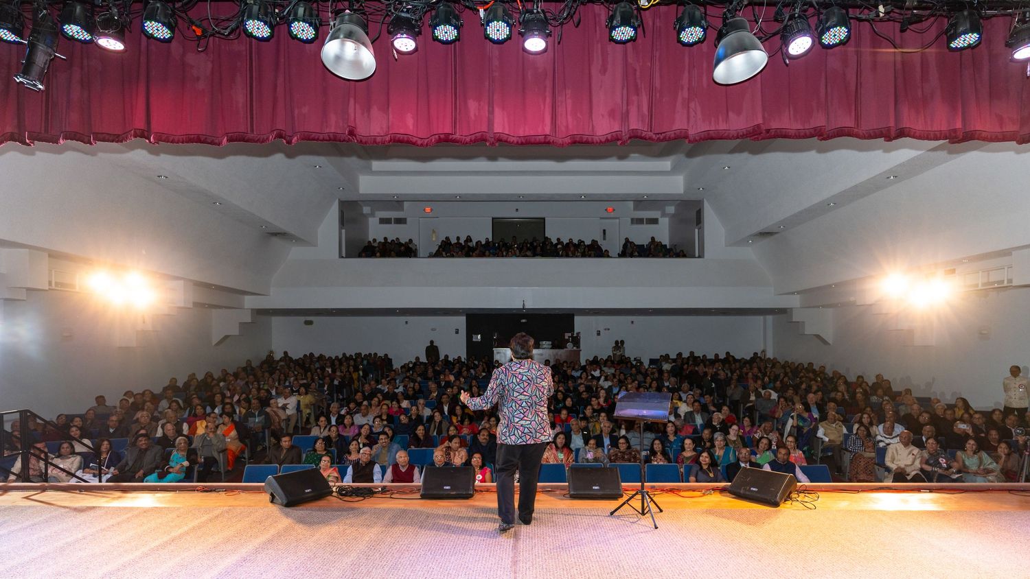 A panoramic view of an indoor sports arena with red curtains, stage lighting, and a large audience in the seating area.