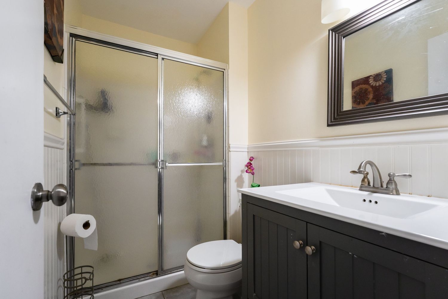 Modern bathroom interior with cream walls, dark wood vanity, and frosted glass shower enclosure.