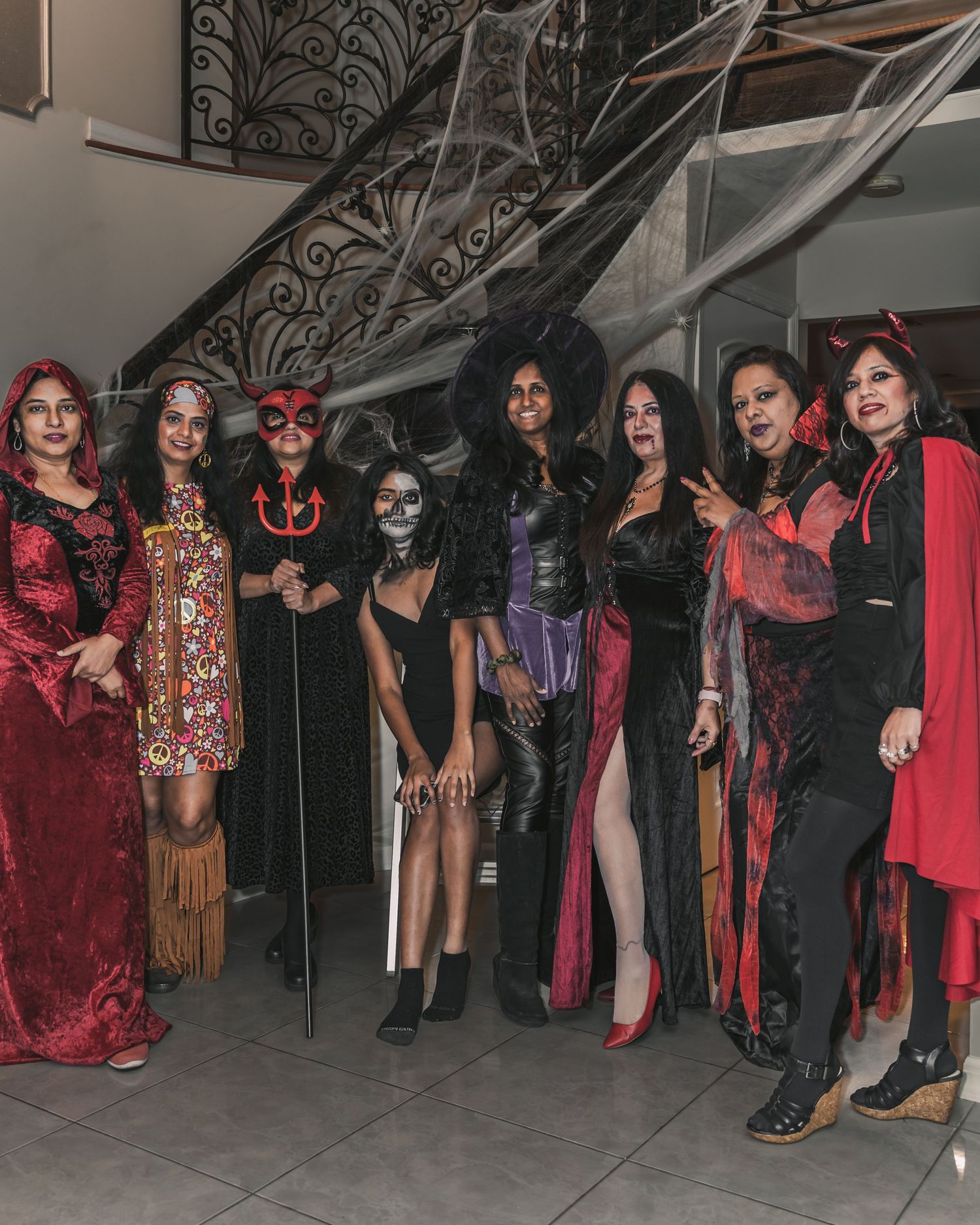 A group of people dressed in gothic Halloween costumes with dark makeup and red and black outfits posing together.