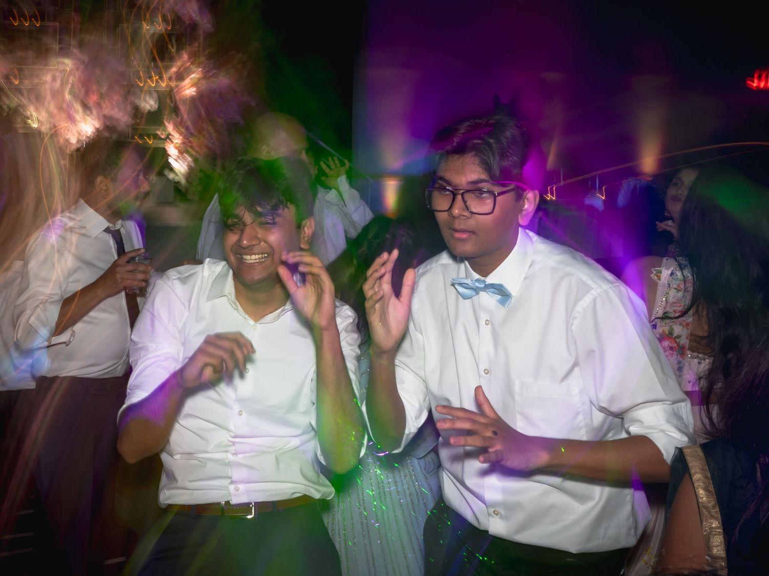 Party guests in formal attire dancing and celebrating under colorful lighting.