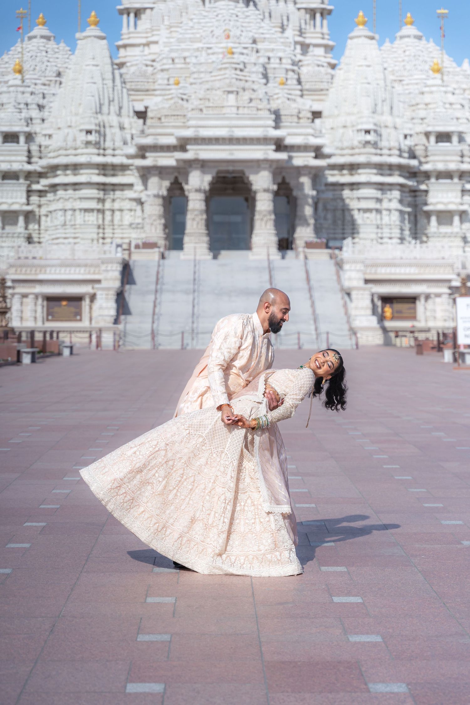 Wedding couple dancing and twirling on marble plaza in front of white temple architecture.