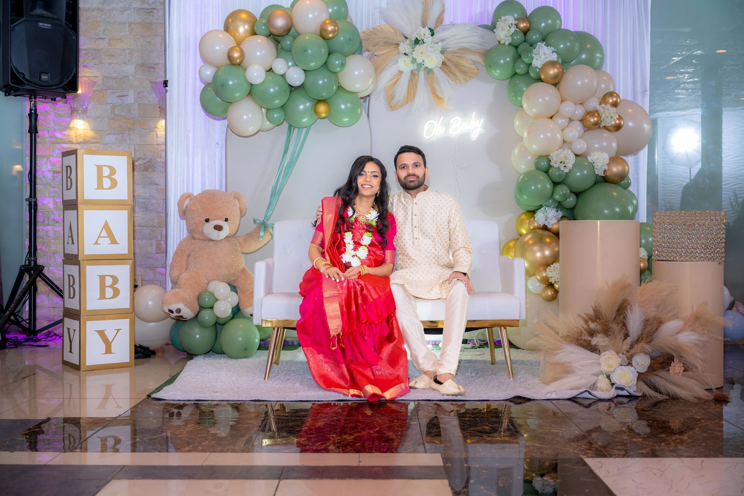 A baby shower celebration setup with green balloon arch, teddy bear decor, and soft pastel colors against a neutral backdrop.