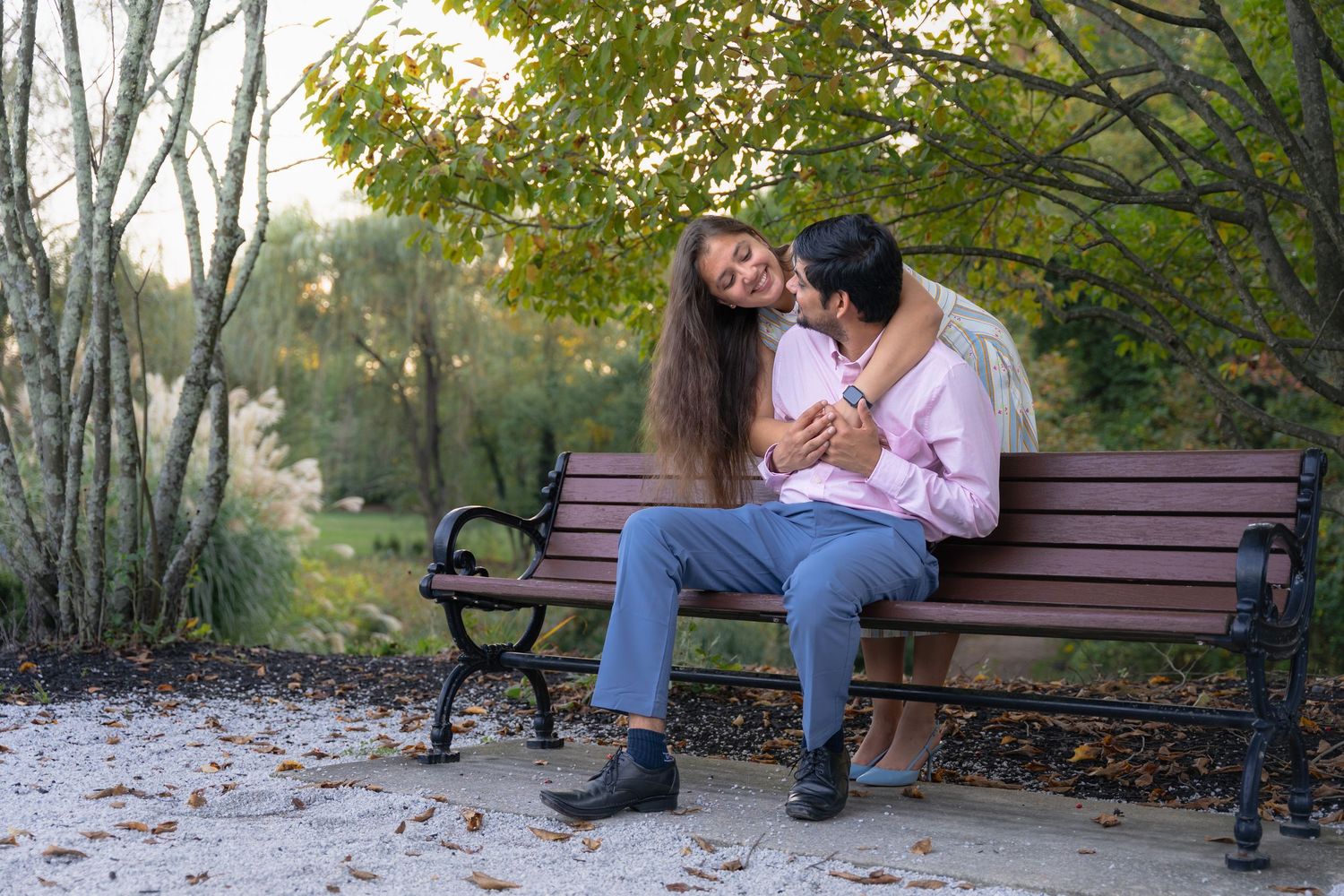 Couple sitting close together on a park bench surrounded by autumn trees.