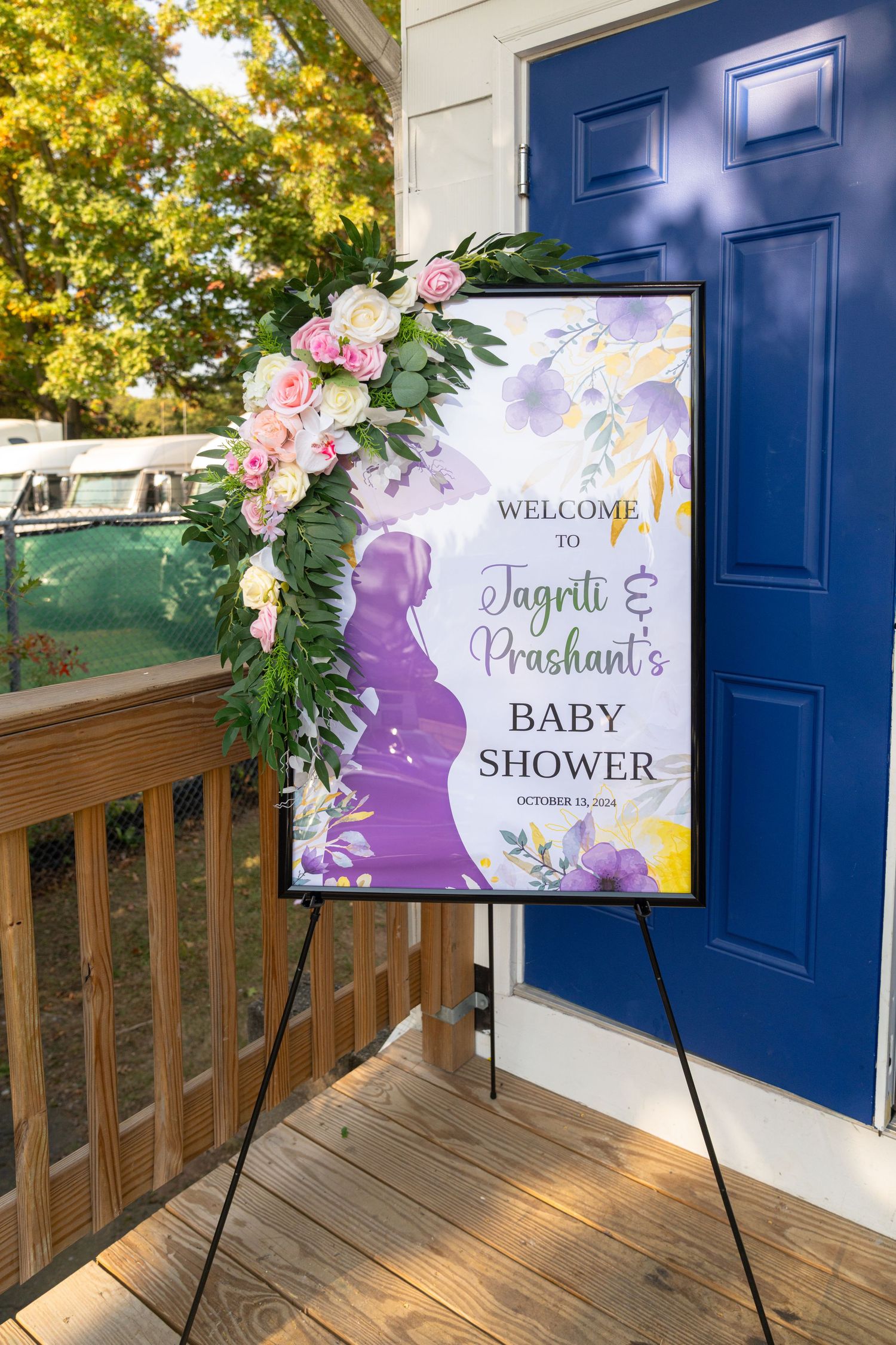 Welcome sign for baby shower decorated with pink flowers against navy blue door.